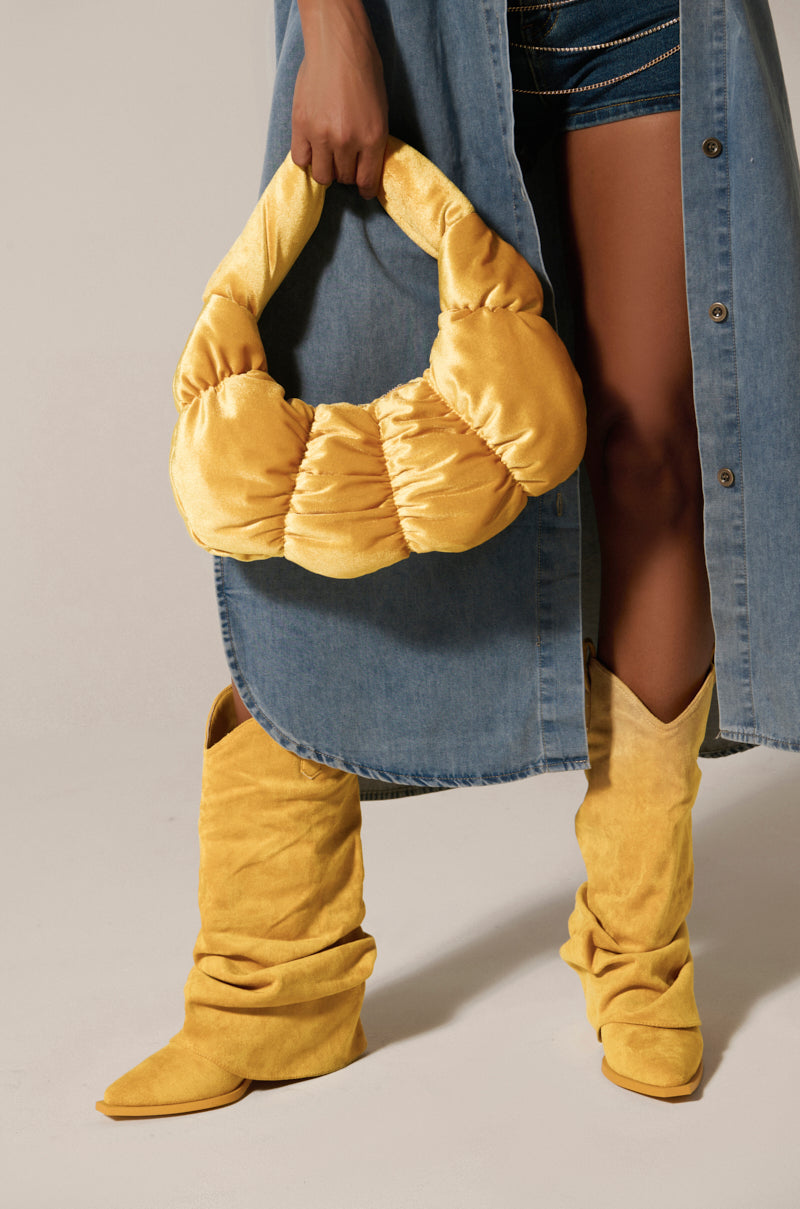 Someone wearing a denim skirt and yellow slouchy boots holds the TRENDY ONE VELVET RUCHED PURSE, perfectly complementing their ensemble. The focus is on the stylish blend of denim with bright yellow accessories. 0