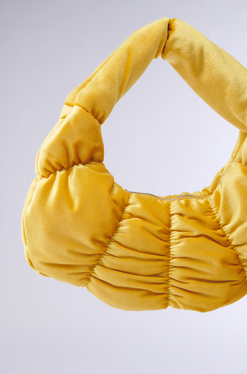 The TRENDY ONE VELVET RUCHED PURSE is a plush, puffy yellow handbag with a crescent silhouette and short handle. Its curved shape enhances the elegant metallic zip-top closure against the plain gray backdrop. 4