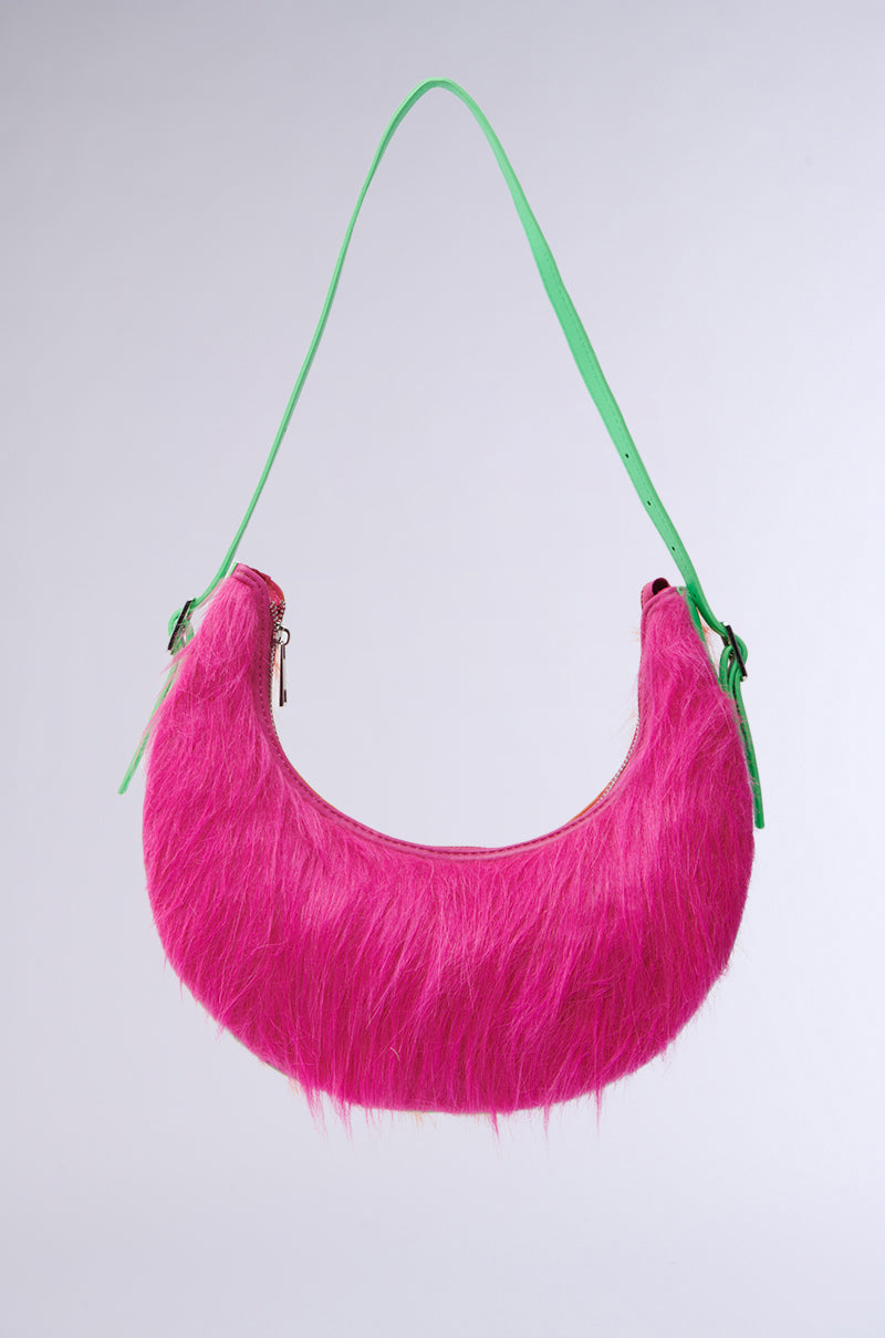 The LETS ALIGN FUR PURSE is a crescent-shaped shoulder bag with vibrant pink faux fur and a contrasting green strap, set against a plain light background.