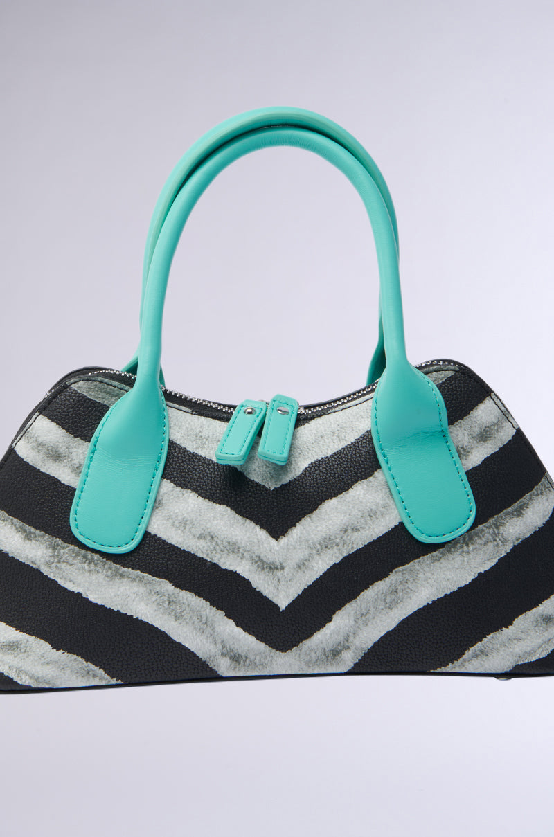 The WILD ONE ZEBRA PU PURSE showcases a black and white zigzag design with bright turquoise handles and accents, crafted from faux leather, displayed on a plain light gray background.