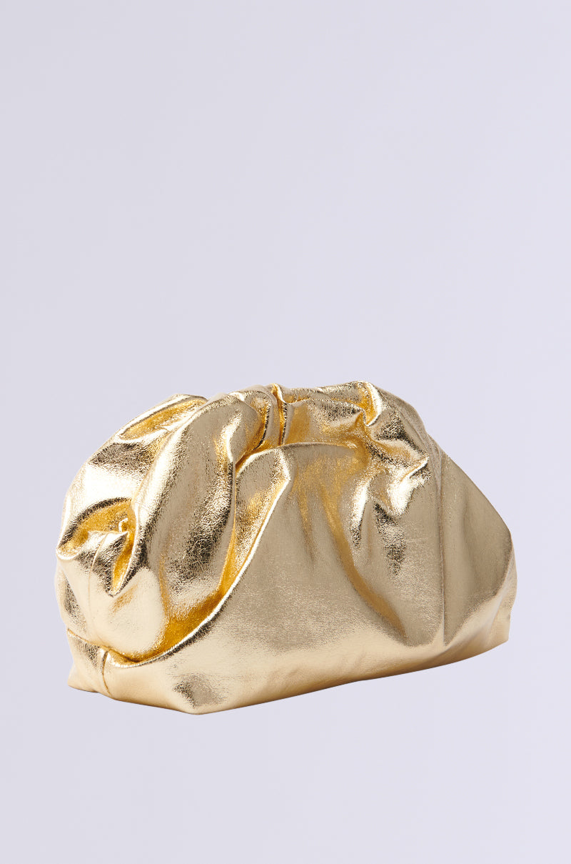 The OVER IT METALLIC CLUTCH, a gold metallic bag with a soft, gathered design and slightly crumpled faux leather texture, is set against a plain gray background, resembling a plush pouch. 2