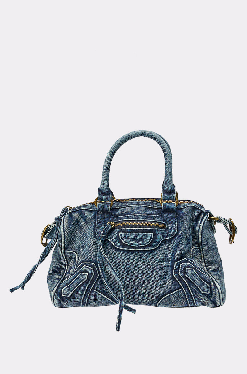 The IM THAT GIRL DISTRESSED PURSE is a blue washed denim handbag with two handles, zipper pockets, decorative stitching, and tassel zipper details—an ideal streetwear accessory shown against a plain white background. 1