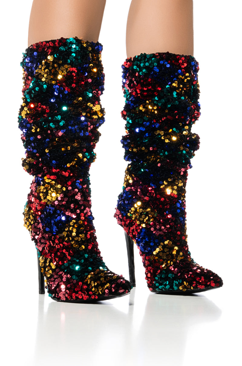 Presenting the AZALEA WANG JIMENA MULTI SEQUIN STILETTO BOOT, a pair of high-heeled, pointed toe boots adorned with multicolored sequins in shades of blue, red, gold, and green. These eye-catching boots feature a slouchy design that's perfectly showcased against a white background.