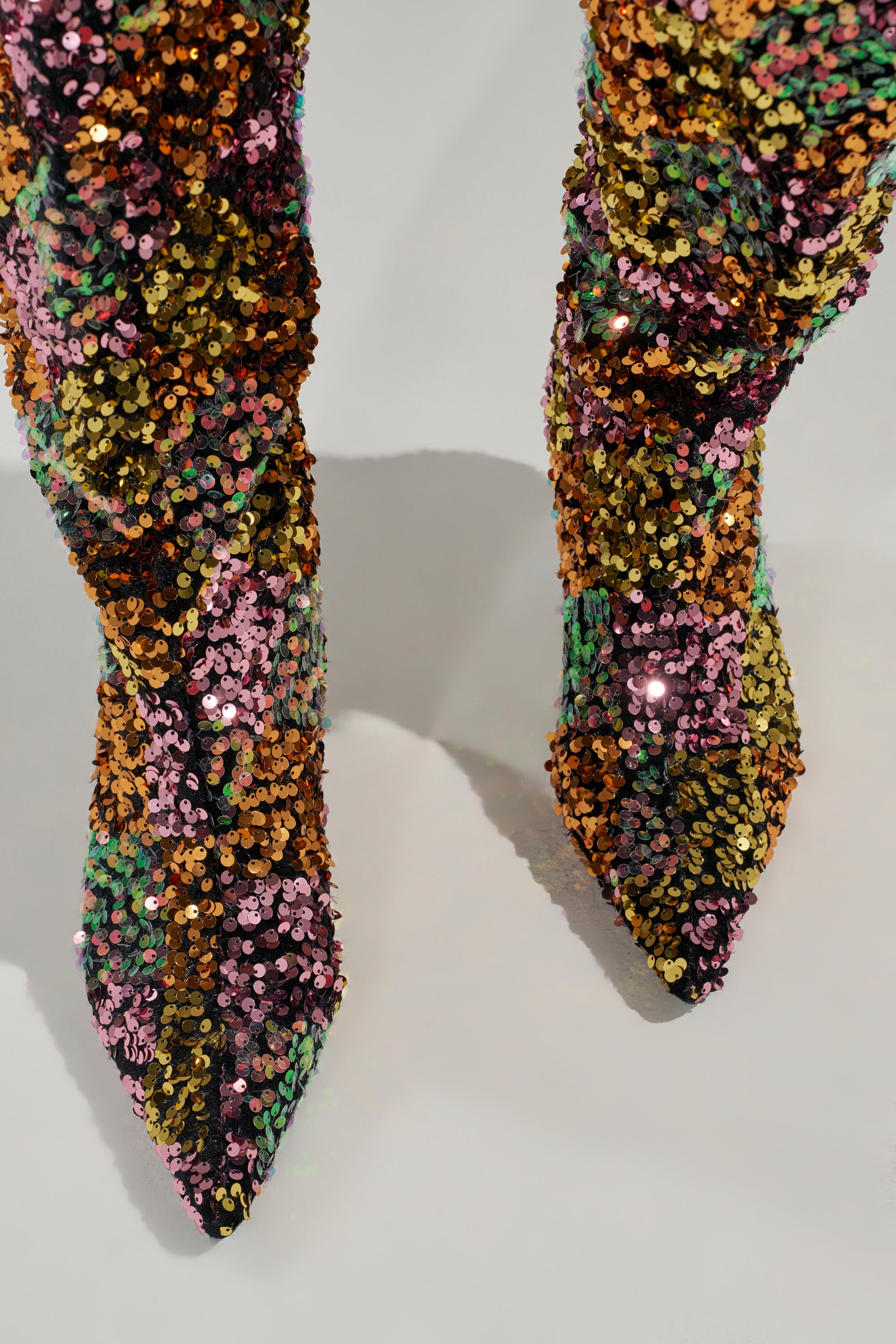 The AZALEA WANG JIMENA MULTI GOLD SEQUIN KNEE HIGH STILETTO BOOT features swirling gold, green, pink, and black sequin patterns on pointy toes. Photographed from above on a light surface, these boots make a bold statement.