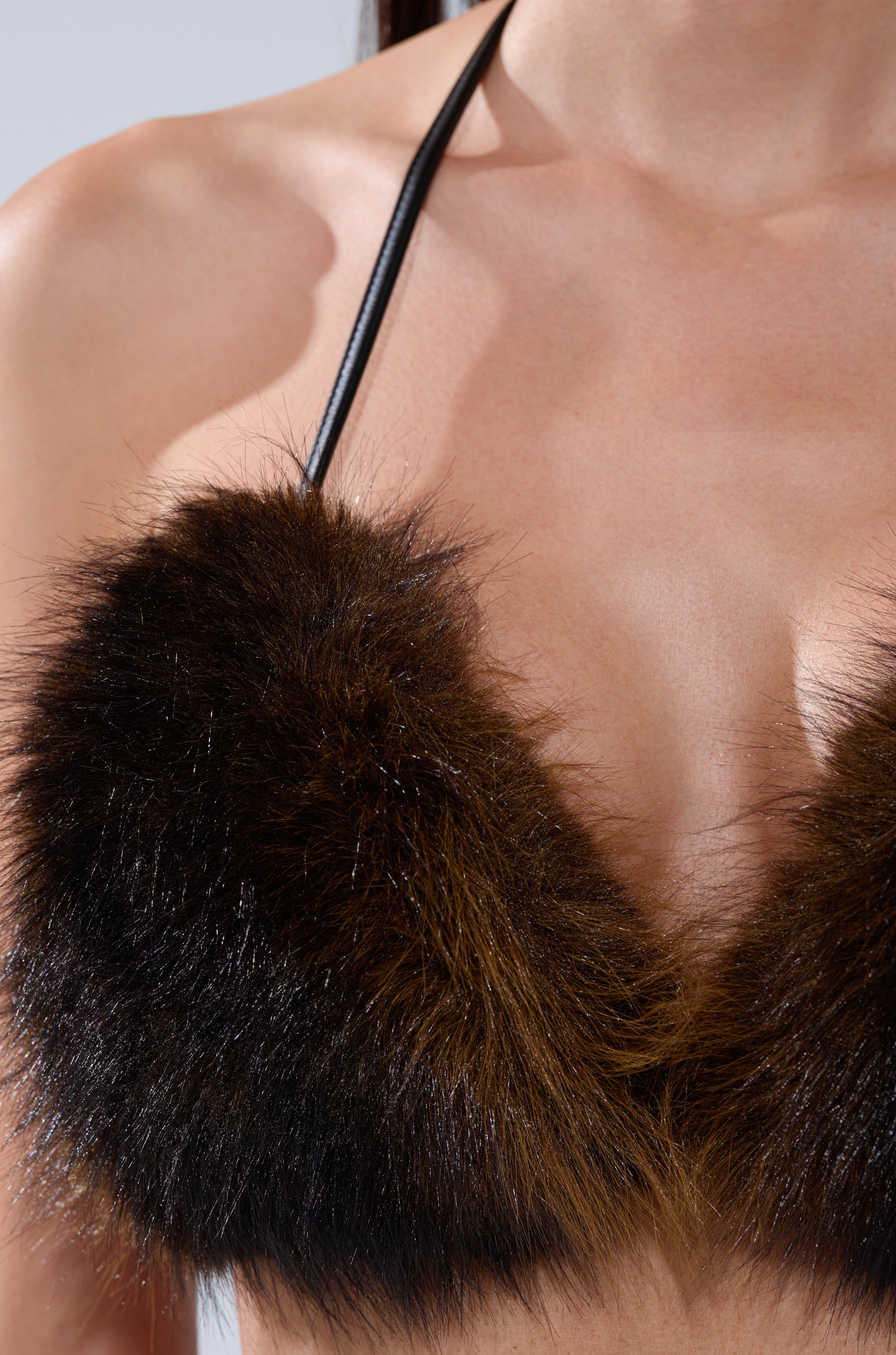 Close-up of a person wearing the BABY ITS COLD OUTSIDE FUR BRALETTE, a brown and black faux fur halter-style top, showing bare shoulders and upper chest against a plain background.