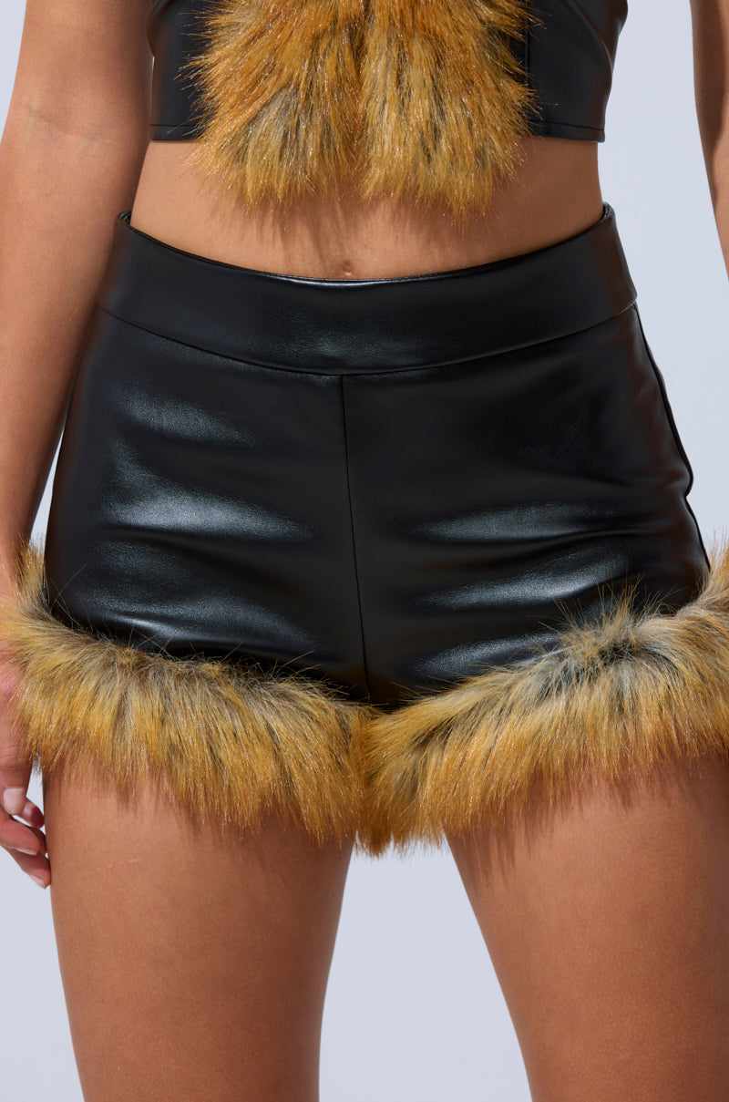 A person wears the DONT TOUCH SHORT WITH FUR TRIM, a high-rise faux leather short with yellow-brown fur trim, paired with a matching crop top. The image is cropped to display only the torso and upper legs. 1