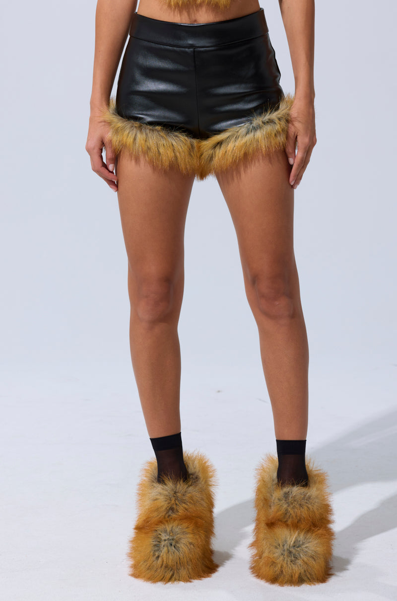 Wearing the DONT TOUCH SHORT WITH FUR TRIM, featuring high-rise faux leather and brown-tan fur accents paired with fluffy matching boot covers, the model poses waist-down against a plain light background. 3