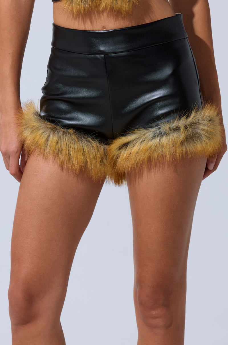 A person wears the DONT TOUCH SHORT WITH FUR TRIM—high-rise faux leather shorts featuring yellow and brown fur around the leg openings. The image is cropped to showcase these statement shorts and the upper legs. 8