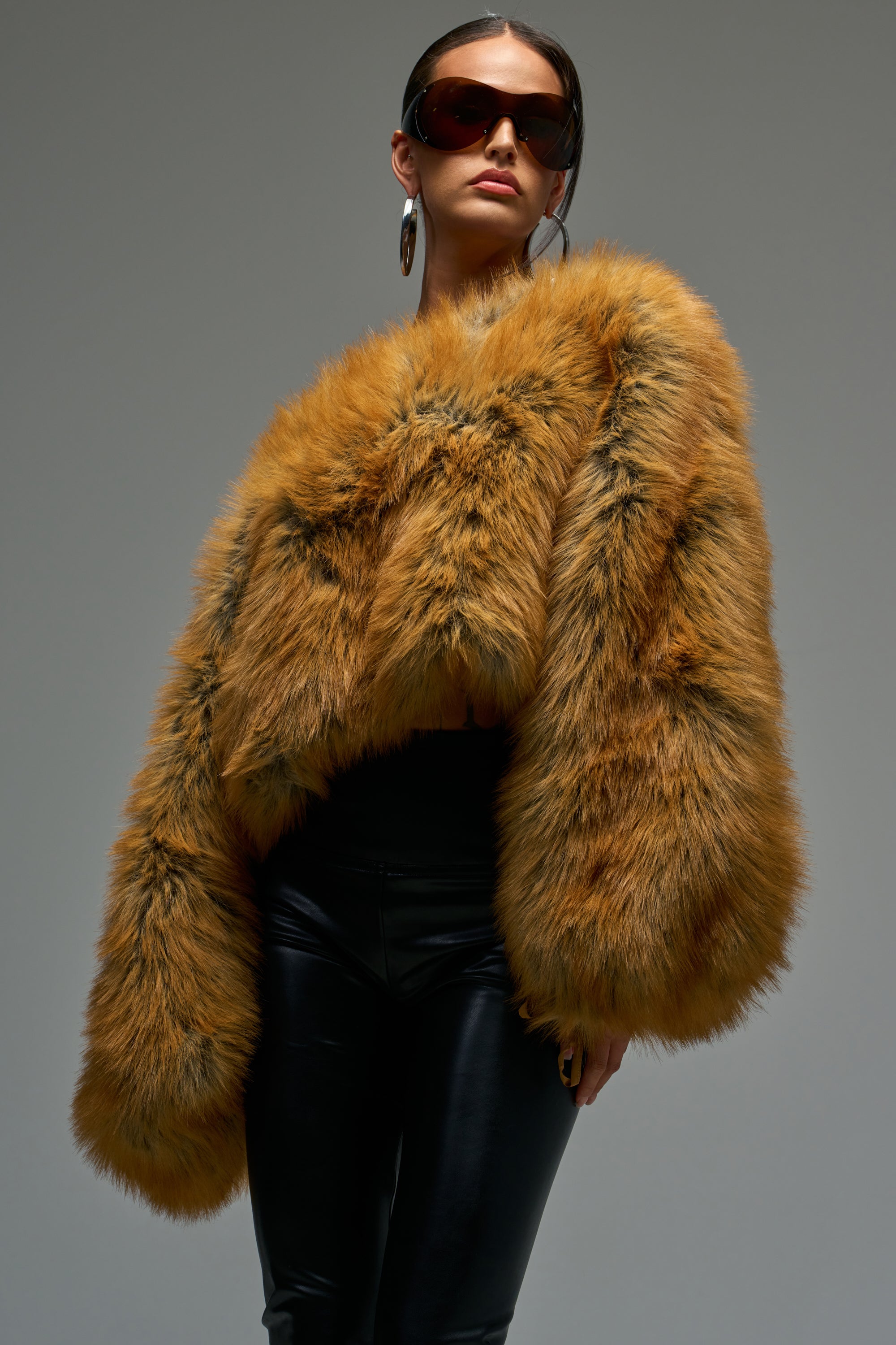 A person in large sunglasses, hoop earrings, and black leather pants exudes après-chic style against a gray background while wearing the SNOW DAY FAUX FUR SWEATER.