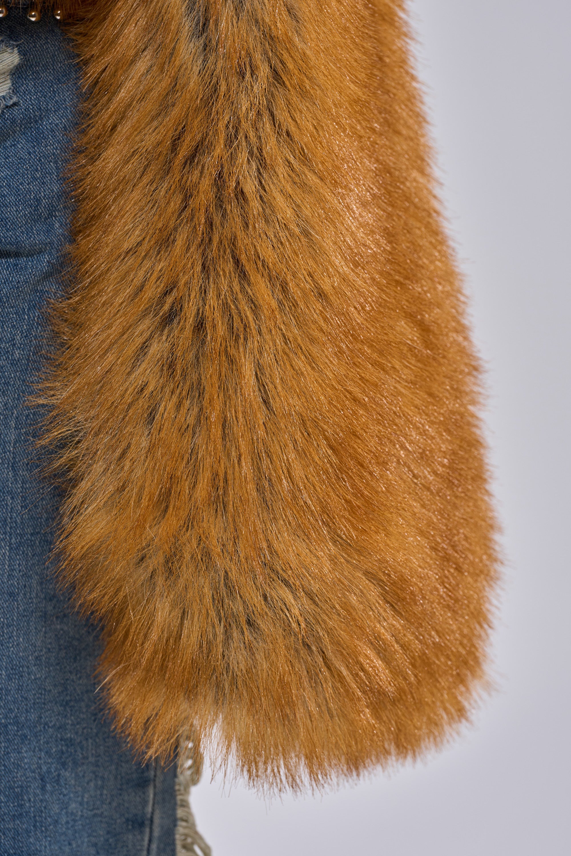 Close-up of a person wearing the SNOW DAY FAUX FUR SWEATER in orange-brown, paired with blue denim jeans.