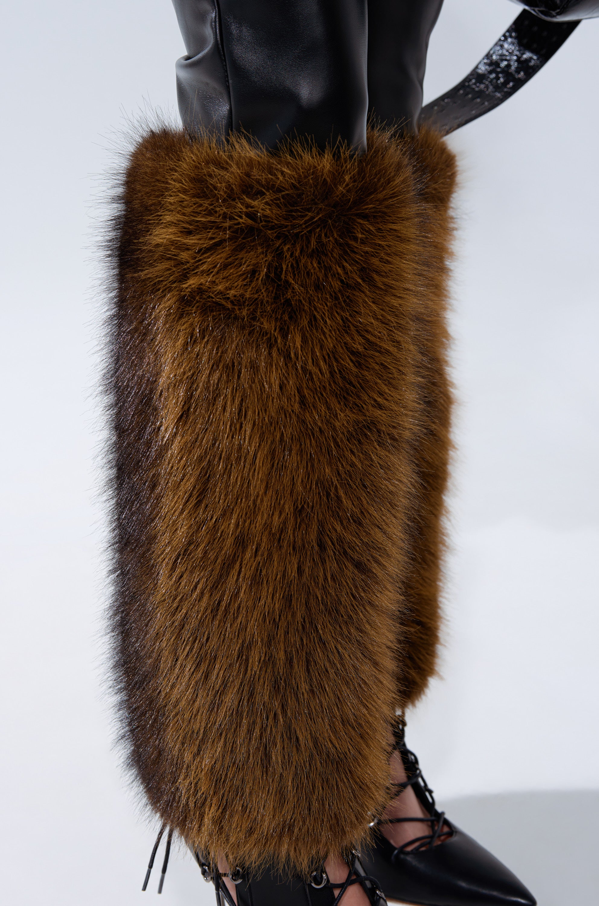 A close-up of a person’s lower legs wearing the BABY ITS COLD OUTSIDE FAUX LEATHER PANT WITH FUR TRIM over black lace-up boots, set against a plain light background.