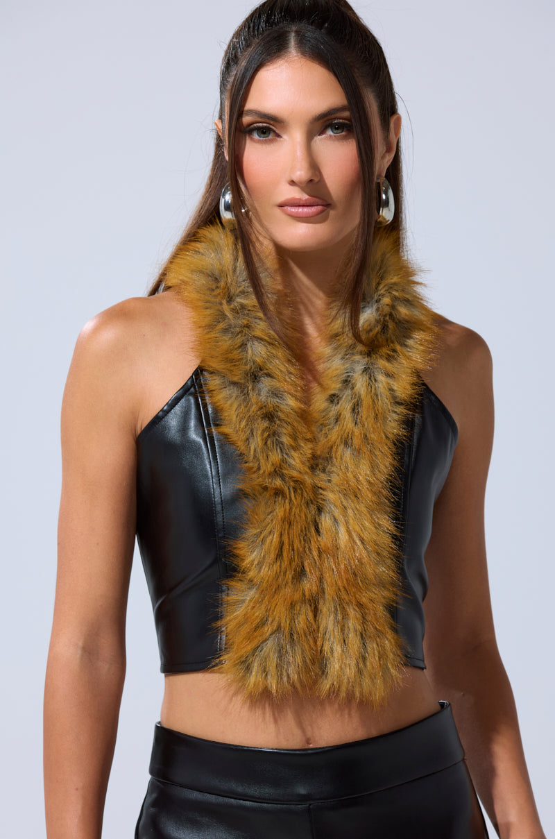 A woman stands against a plain light background in the DONT TOUCH FUR BRALETTE crop top and pants, paired with a brown and black faux fur scarf. Her long brown hair is styled in loose waves. 1