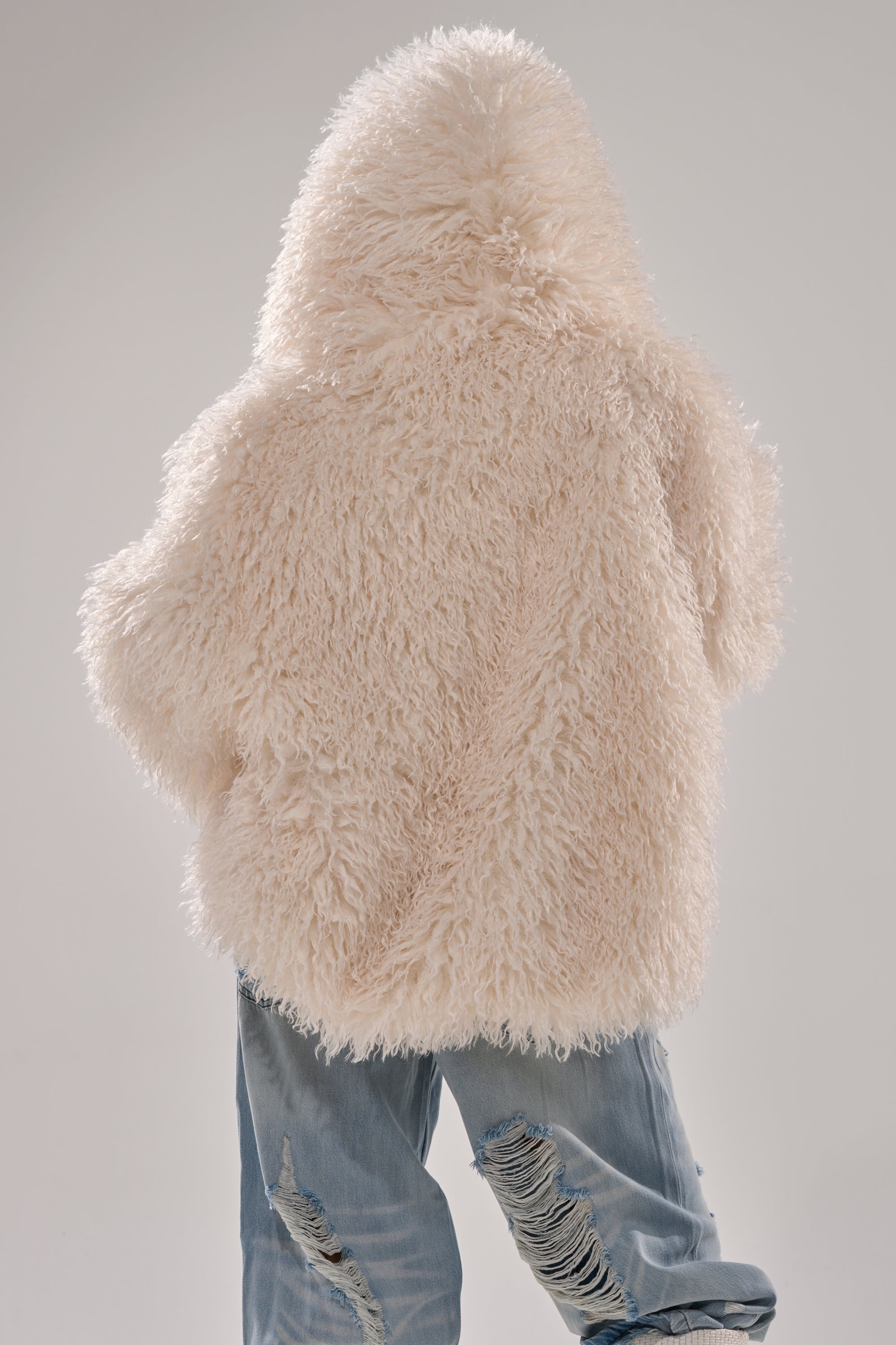 Photographed from behind against a plain background, a person wears the LOOK AT ME NOW HOODED FUR BOMBER IN IVORY paired with distressed, light-wash jeans. 9