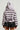 The image features a person from behind wearing the MINA FAUX FUR BOMBER, which has an oversized silhouette with plush, striped faux fur and includes a hood. The jacket is paired with a short black skirt, set against a plain, neutral background.