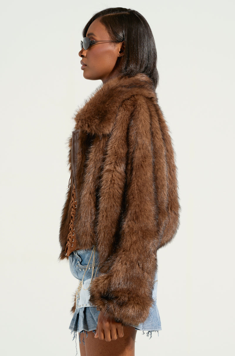 A person in KAI FAUX FUR BOMBER sunglasses steps into view, styled with straight, shoulder-length hair and a trendy short denim skirt featuring a metallic silver zip, against a simple backdrop.
