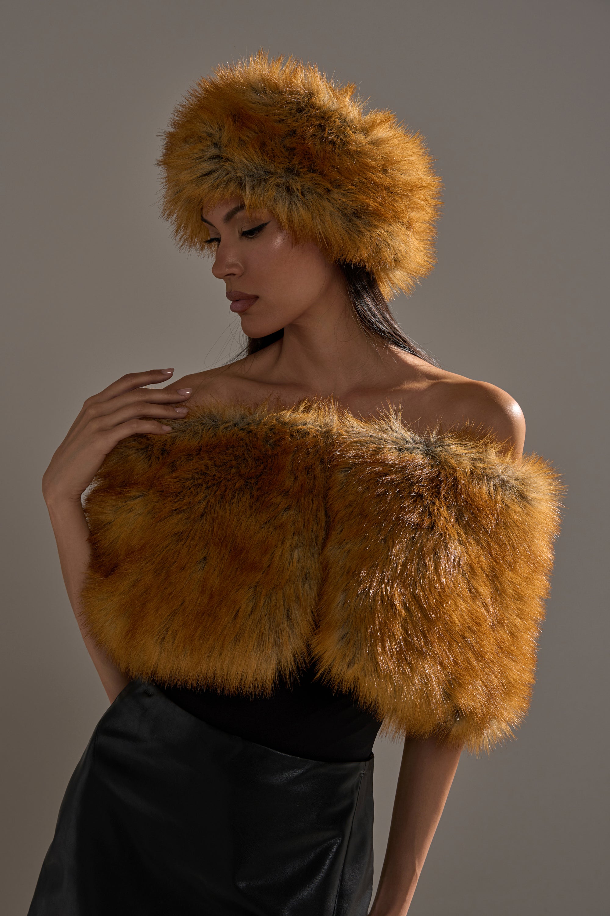 A glamorous woman models the REALLY LIKE THAT FAUX FUR SHAWL, a vintage-inspired, off-the-shoulder piece in golden-brown, elegantly posing with a matching hat against a neutral background.