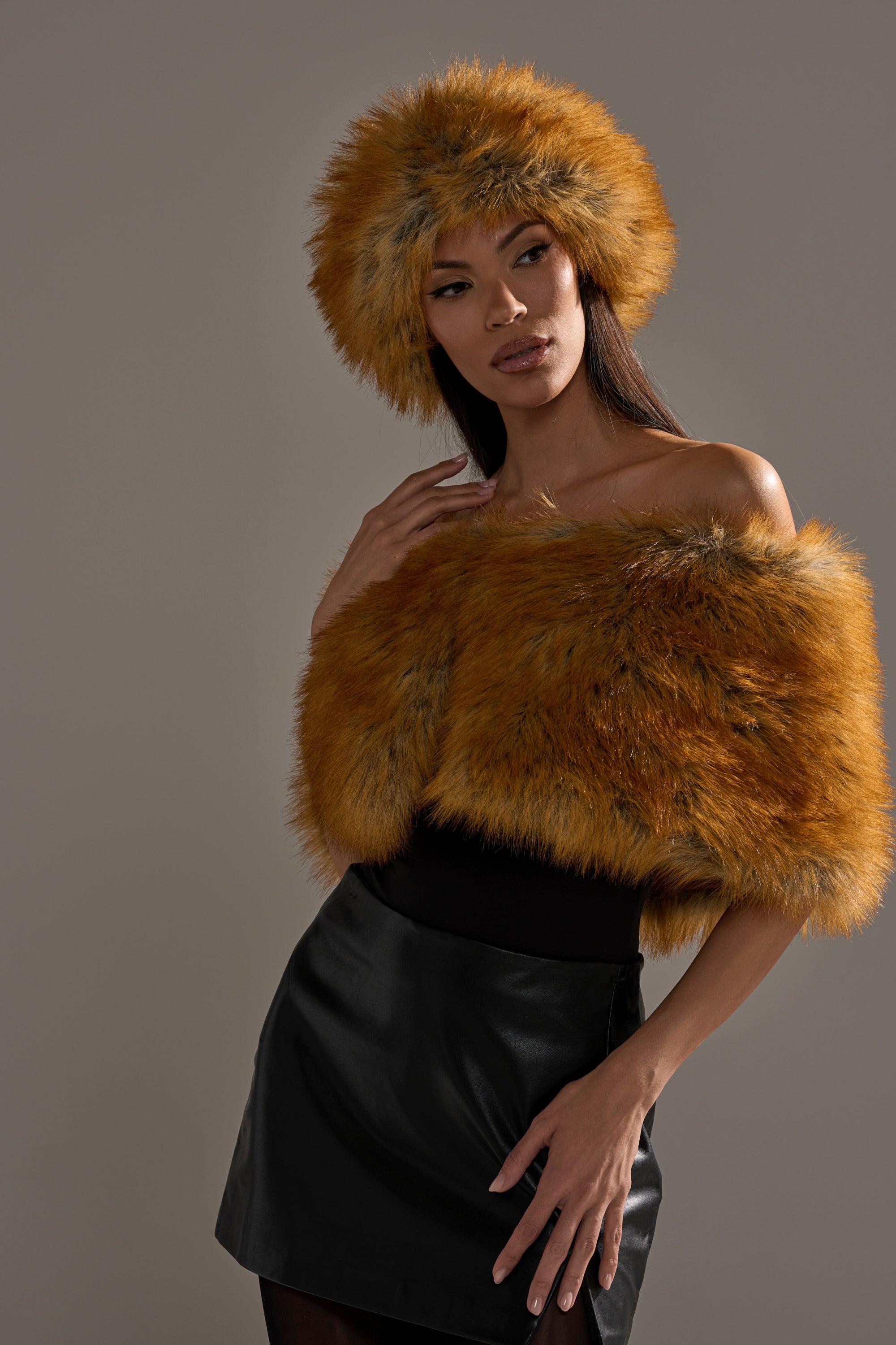 A woman poses with one hand on her hip, wearing a vintage-inspired orange-brown faux fur hat, a black mini skirt, and the REALLY LIKE THAT FAUX FUR SHAWL against a plain gray background. 1