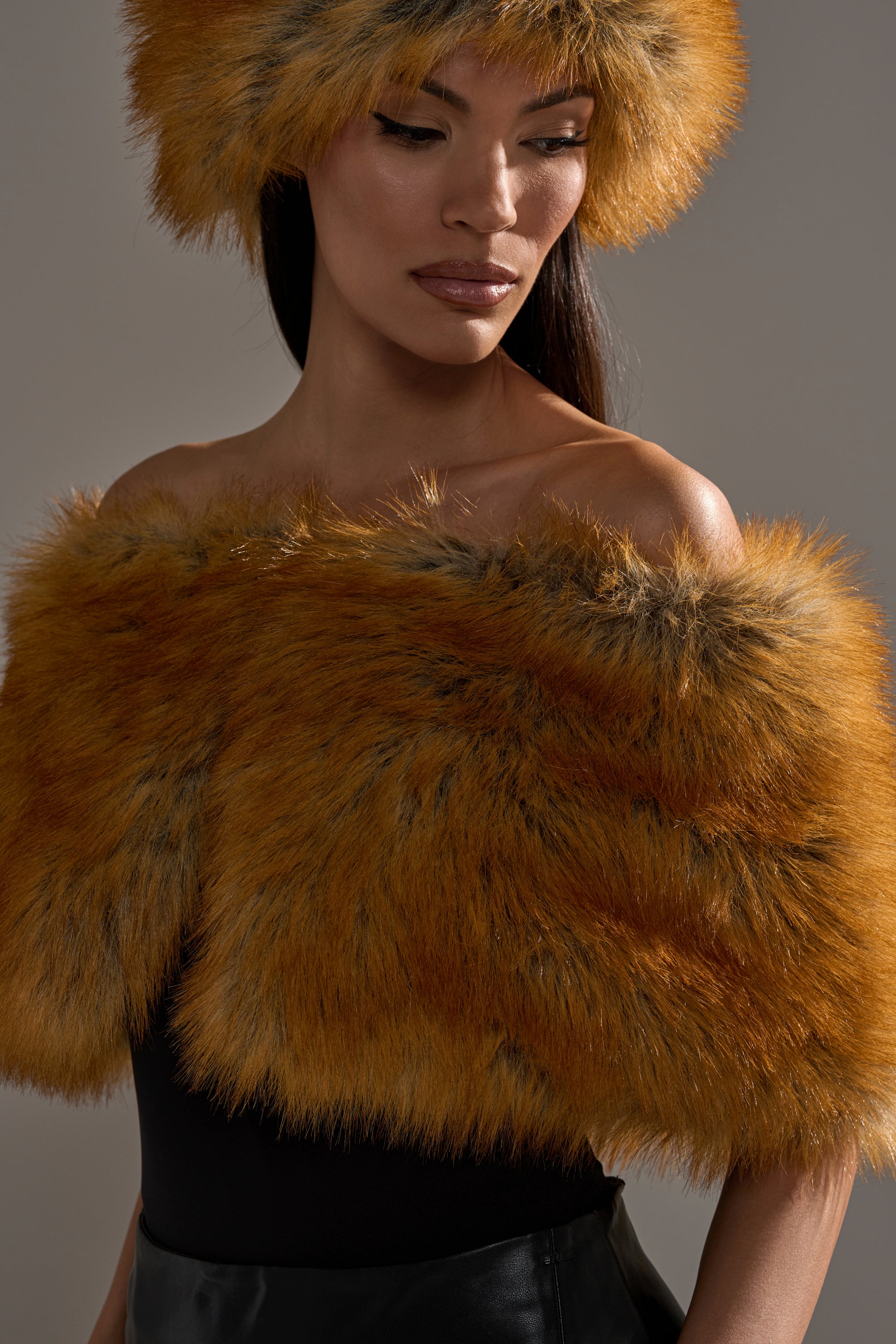 A woman wears the REALLY LIKE THAT FAUX FUR SHAWL and a matching fur hat over a black strapless top, looking downward with a neutral expression against a plain gray background. 2