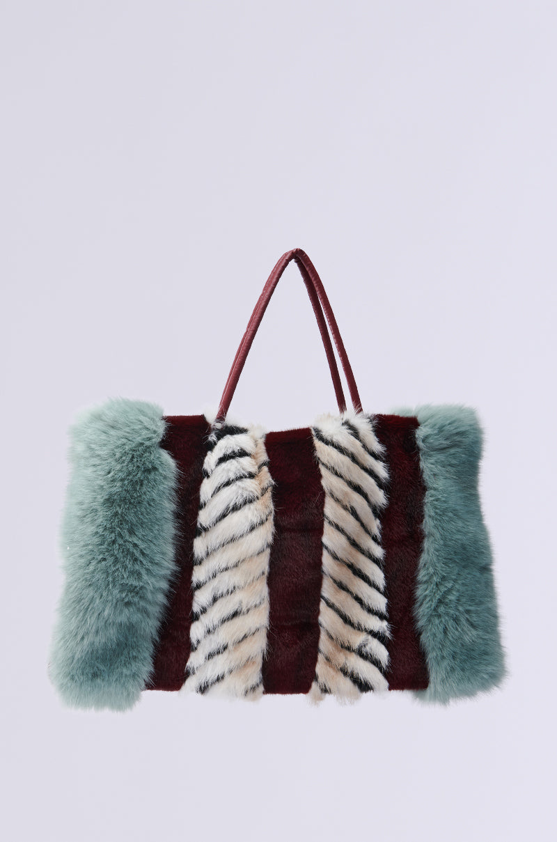 The HAVE IT ALL FAUX FUR TOTE is an oversized fashion-forward handbag with fluffy faux fur panels. It boasts a striking color block pattern in green, maroon, and black-and-white stripes, complete with two thin handles for convenient carrying. 1
