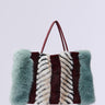 The HAVE IT ALL FAUX FUR TOTE is an oversized fashion-forward handbag with fluffy faux fur panels. It boasts a striking color block pattern in green, maroon, and black-and-white stripes, complete with two thin handles for convenient carrying.