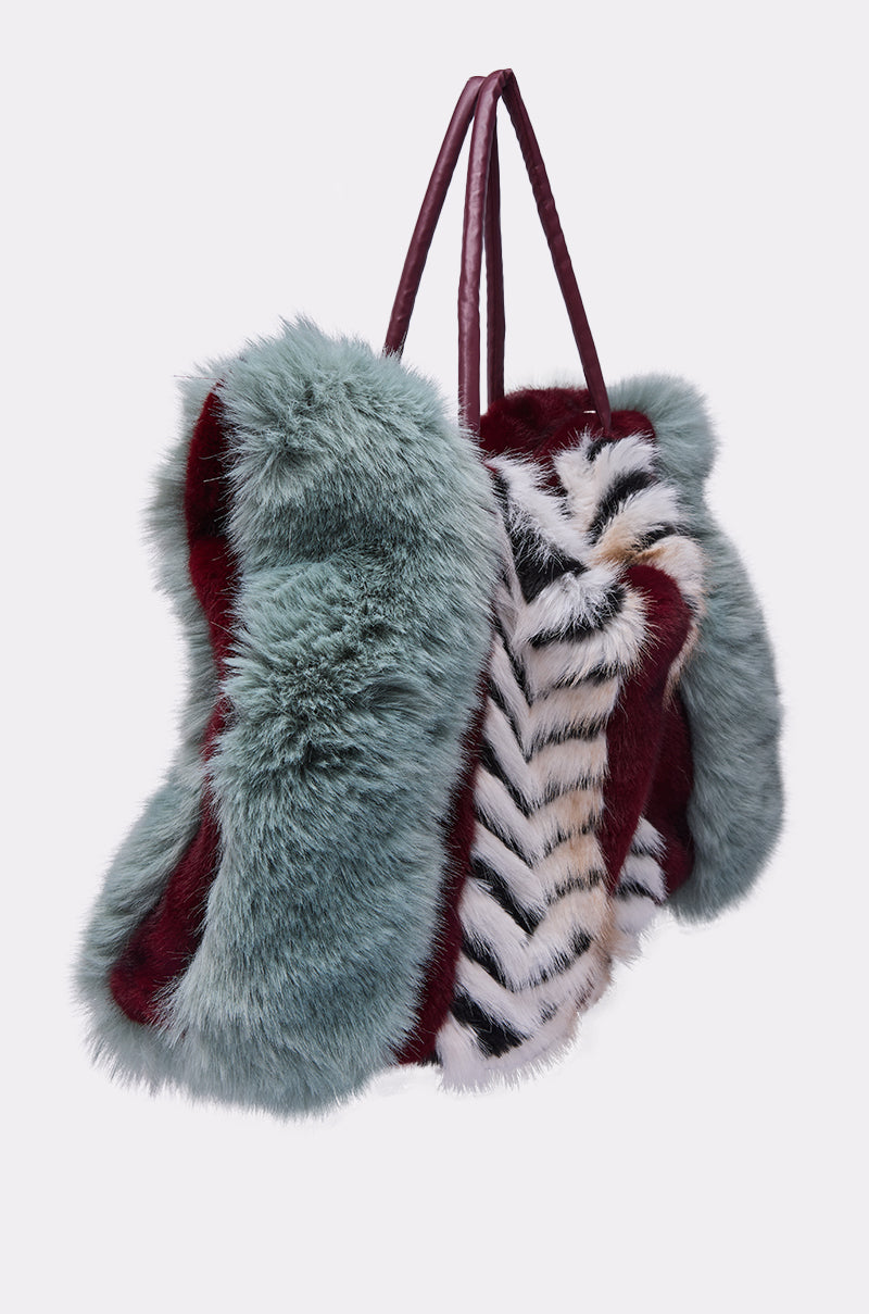 The HAVE IT ALL FAUX FUR TOTE is an oversized handbag in vibrant teal, burgundy, white, and black chevron faux fur with sturdy burgundy handles—a bold color block tote for standout style.