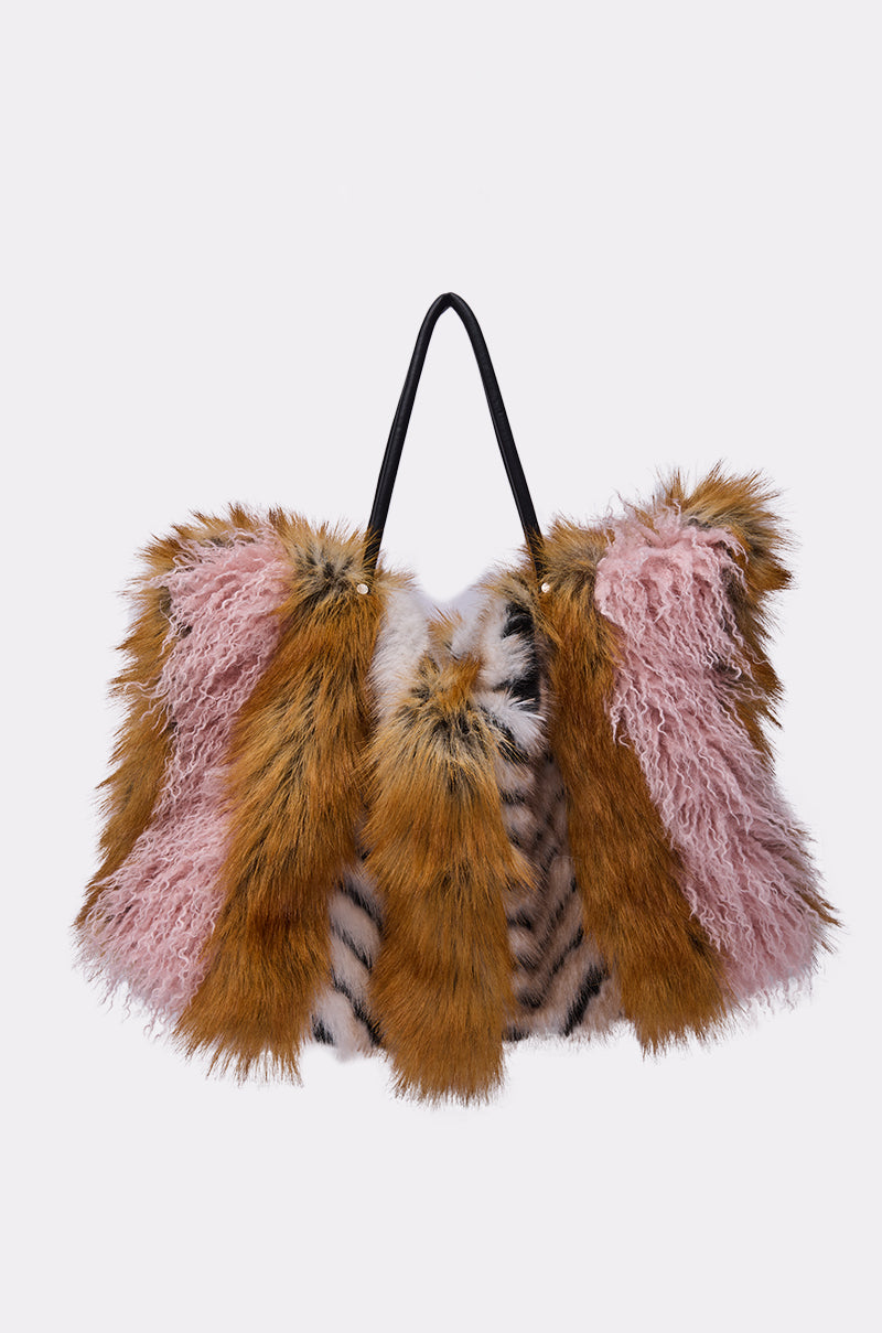 The WILD ONE FAUX FUR TOTE, an oversized bag with pink, brown, and white faux fur panels and a thin black shoulder strap, stands out against a plain background. 0