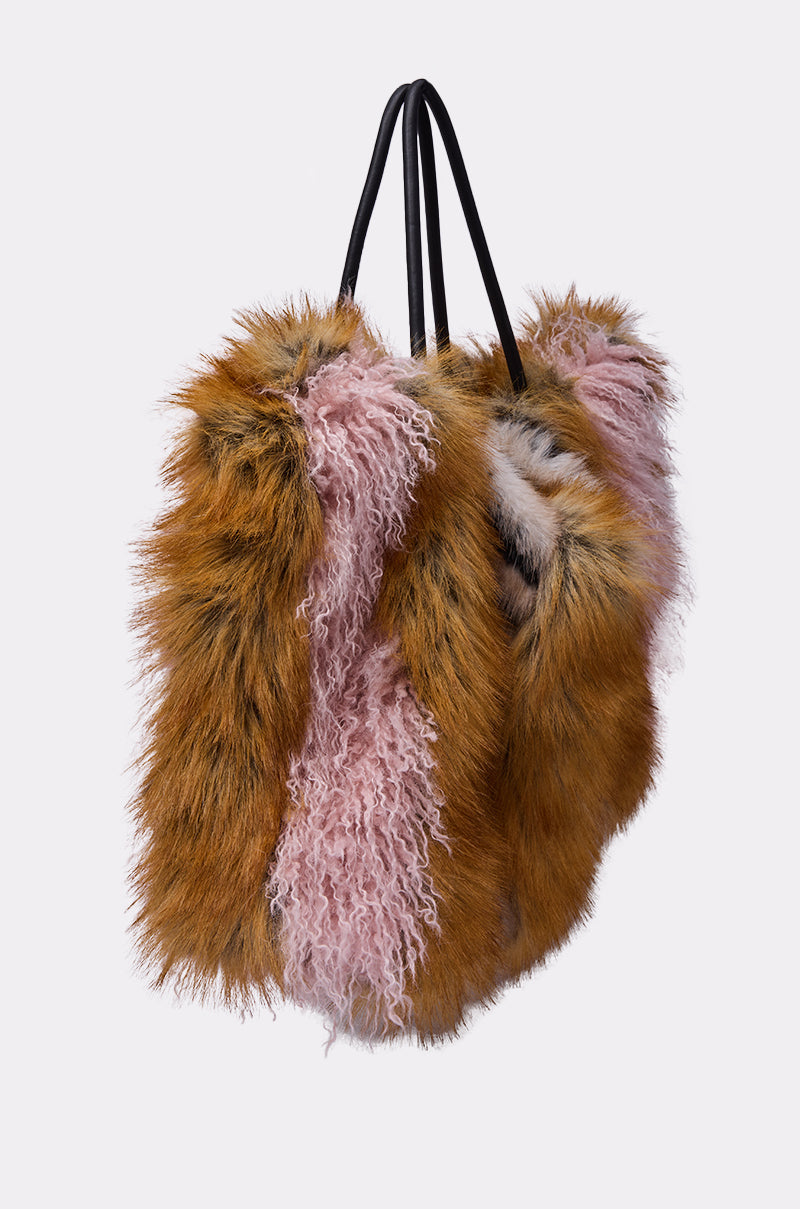 The WILD ONE FAUX FUR TOTE features long black handles, a satin-lined interior, and is covered in fluffy brown and pink faux fur, shown against a light grey background. 2