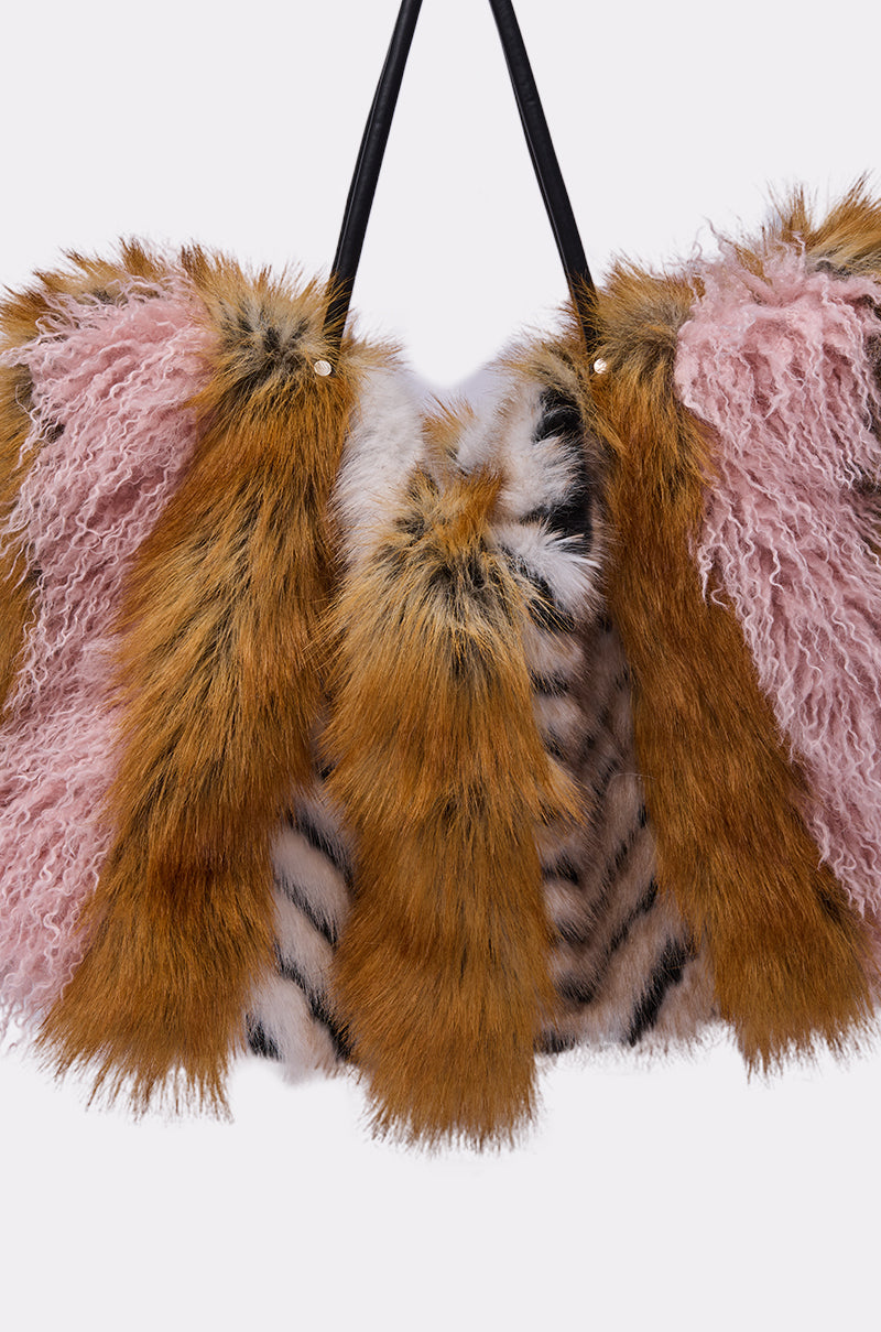 The WILD ONE FAUX FUR TOTE is an oversized handbag with alternating panels of brown faux fur, pink curly faux fur, and white fur with black stripes, designed with two black handles. 3