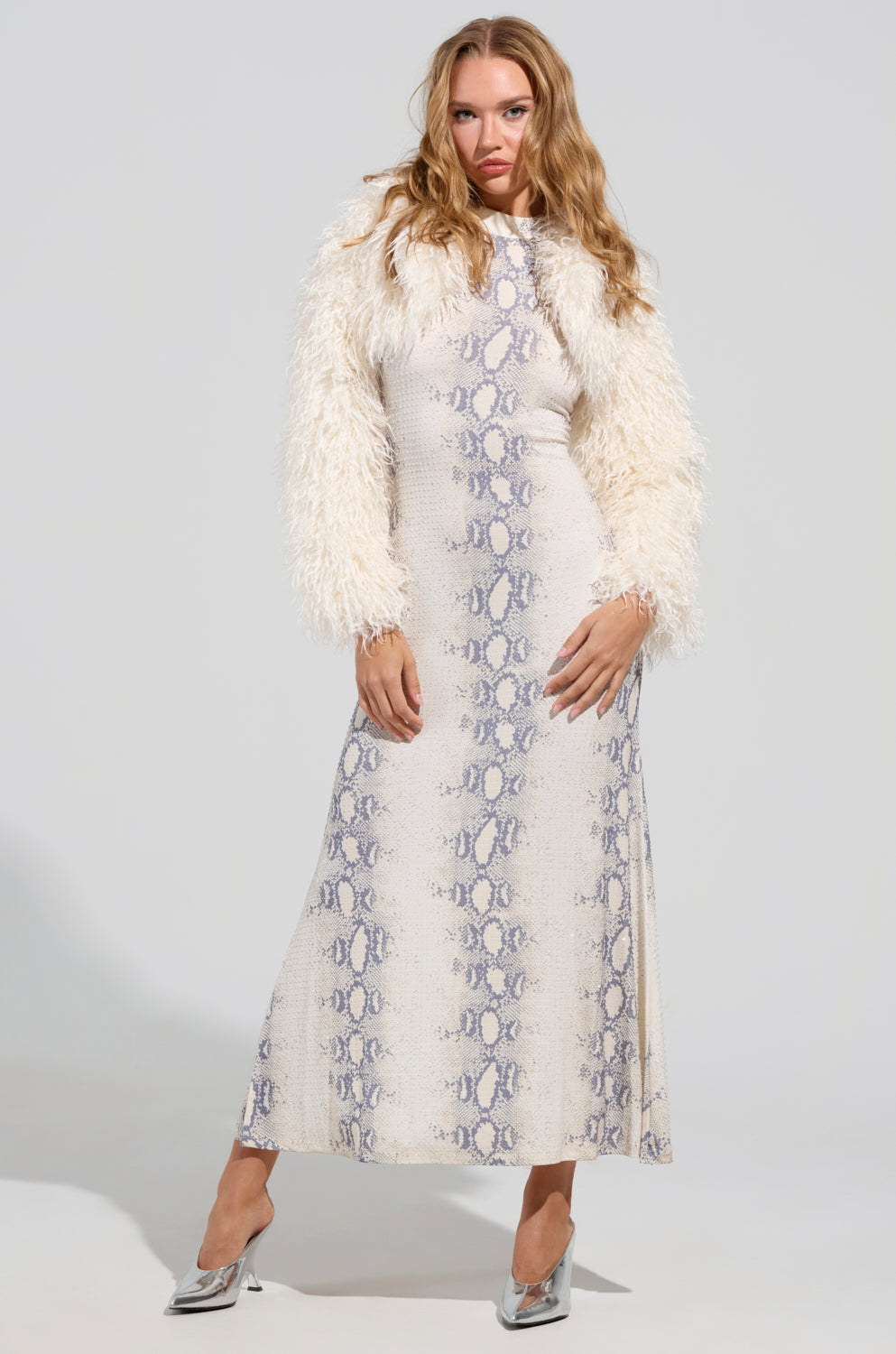 A person wearing a long, patterned dress complemented by LILIANA ULTRA CROP FAUX FUR booties poses confidently against a neutral background.