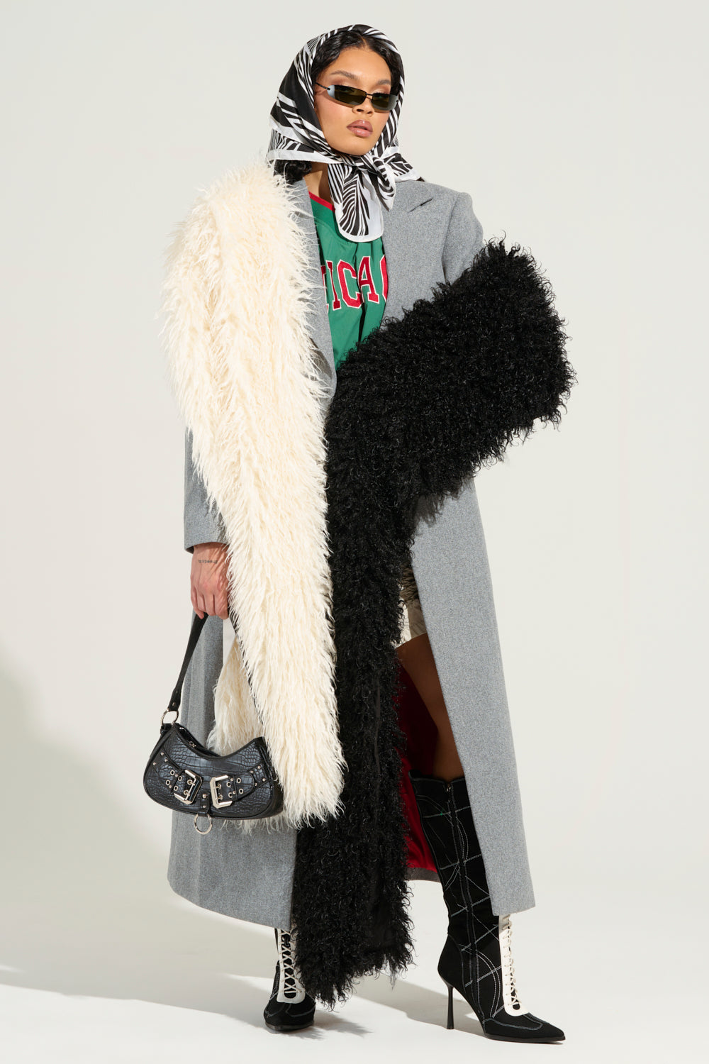 A fashionable individual sporting sunglasses and a headscarf styles a gray coat over a red shirt. They clutch a black handbag and flaunt knee-high black boots with white laces, their look completed by the EPIC DREAMS FAUX FUR SCARF draped gracefully over one arm.