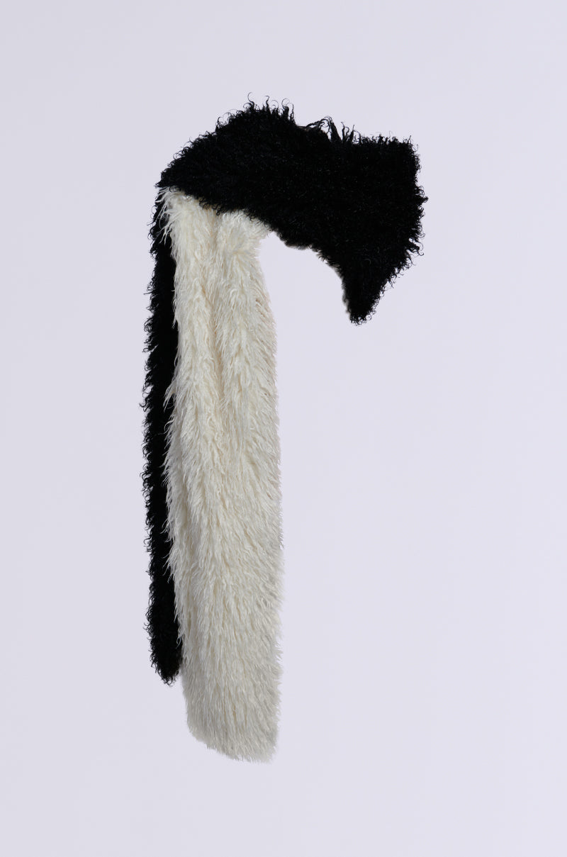 The EPIC DREAMS FAUX FUR SCARF, with its elegant black and white color block pattern, gracefully flows in the air. The black section rests on top with the white below, set against a plain white background that accentuates its chic design.
