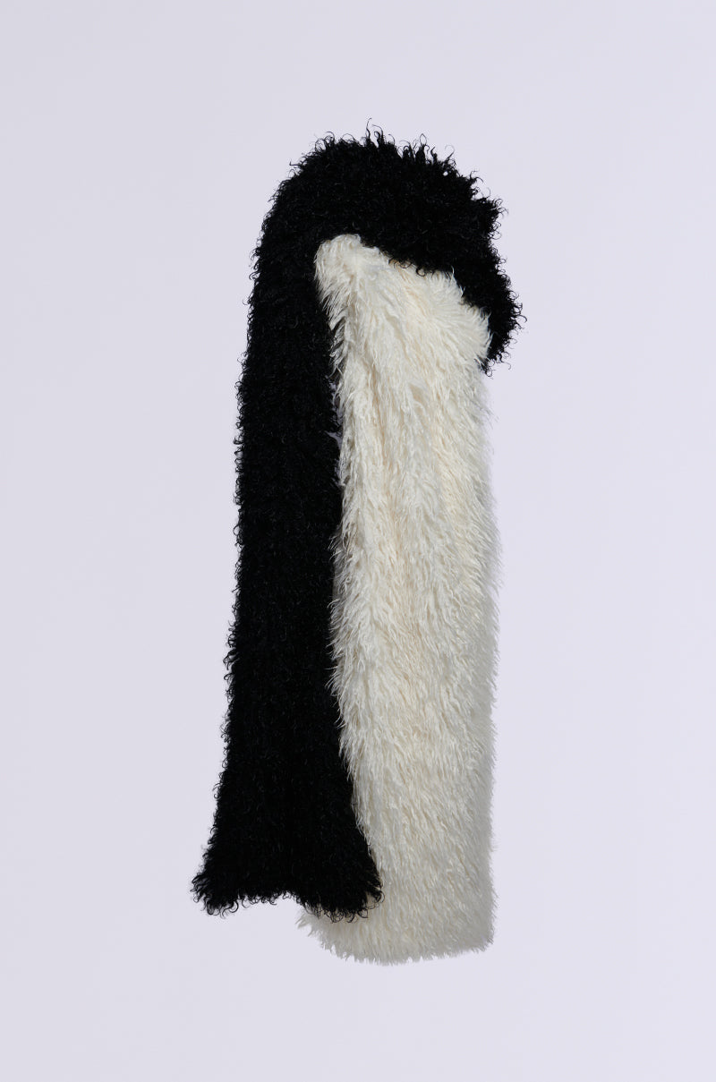 The EPIC DREAMS FAUX FUR SCARF, featuring a fuzzy faux fur material and a color block pattern, is displayed against a white background. The left section is black and the right section is ivory, highlighting its textured, shaggy look.