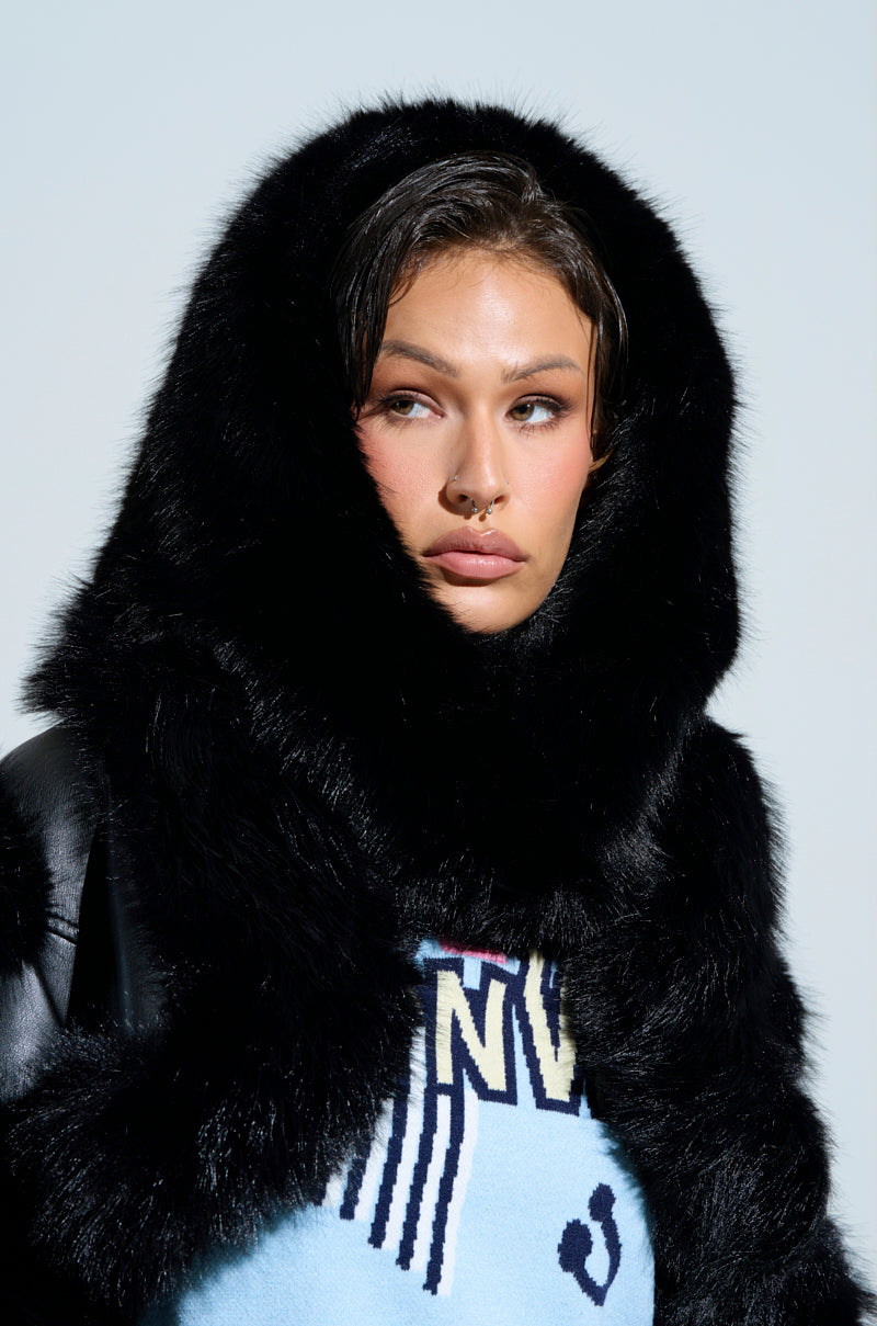 Wearing the IM THE ONE FAUX FUR HOOD, a person with short hair and a nose piercing exudes luxury fashion. They're styled in a blue graphic sweater, looking to the side against a light background. 0