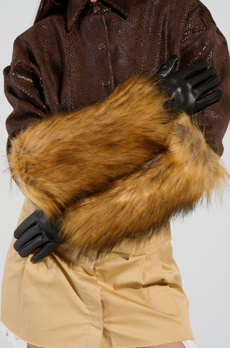 A person wearing a brown textured jacket and beige skirt poses with arms crossed, accessorized with the GRACELLE EXTENDED FAUX FUR GLOVES and black gloves, creating a stylish and fashionable winter accessory look. 1