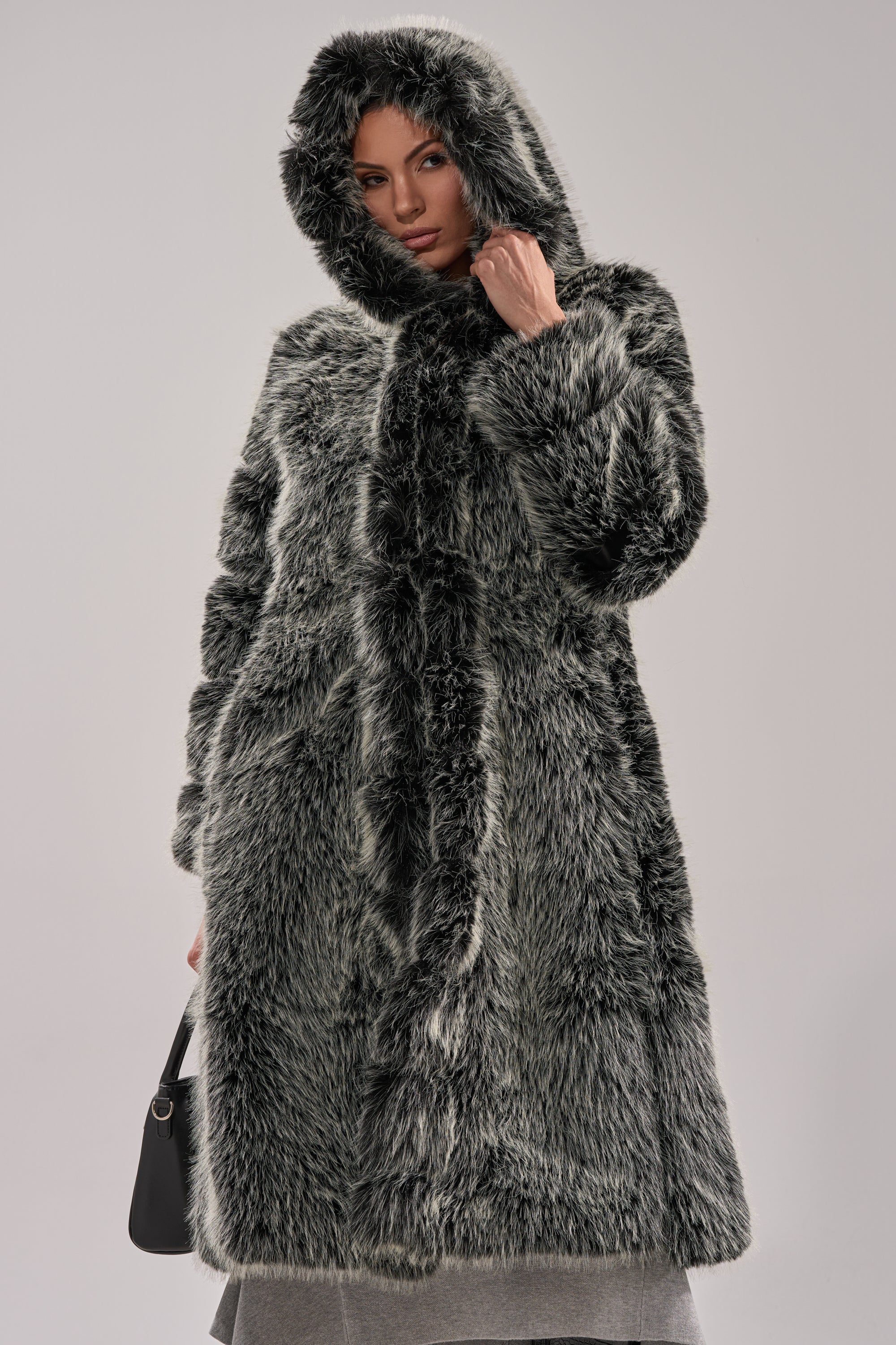 A person models the SNOW BUNNY HOODED FAUX FUR COAT in grey and black, holding a black handbag against a plain light background.