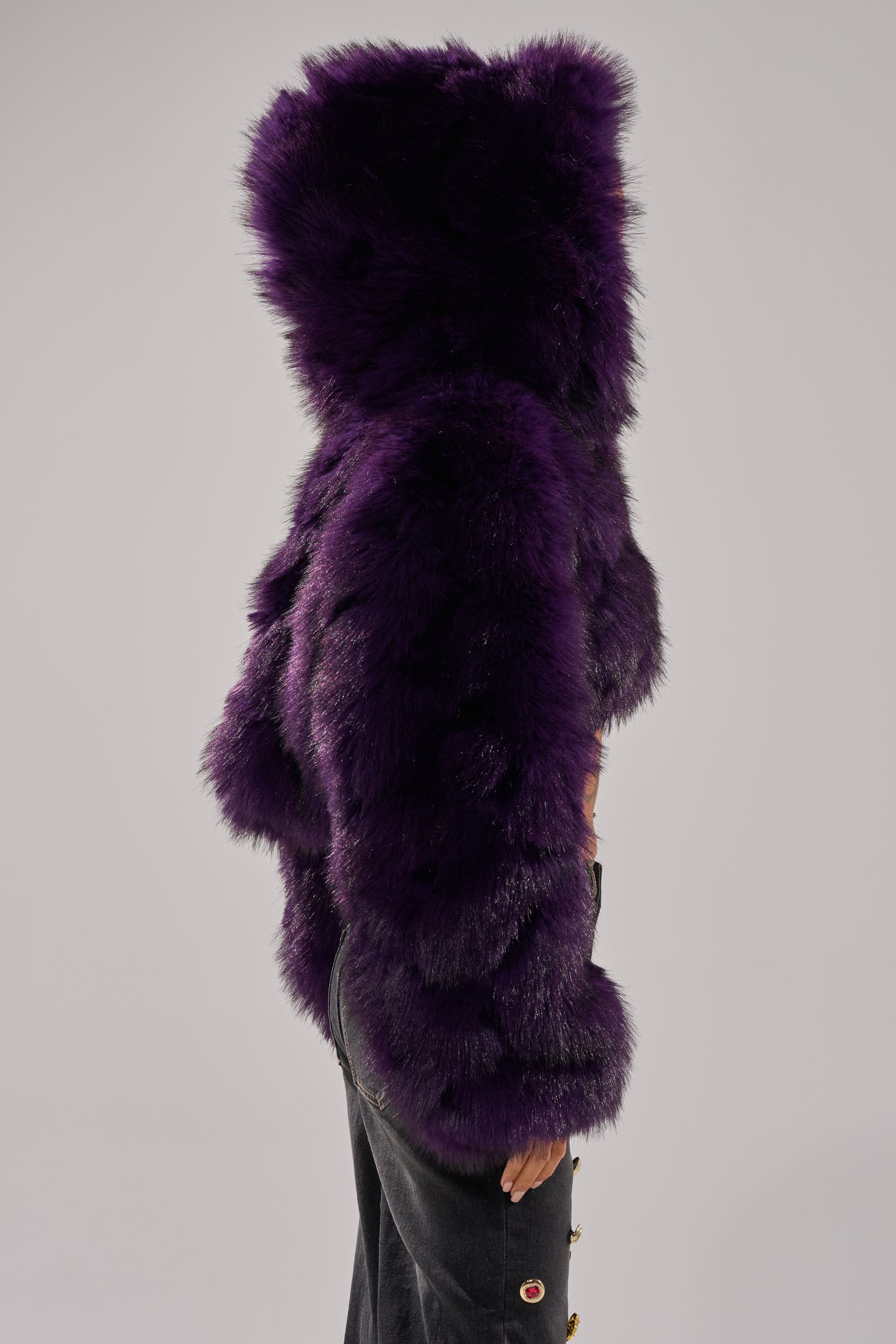 A person stands in profile wearing the JUST A FLING CROPPED FAUX FUR jacket in deep purple and dark pants with visible buttons against a plain light background.