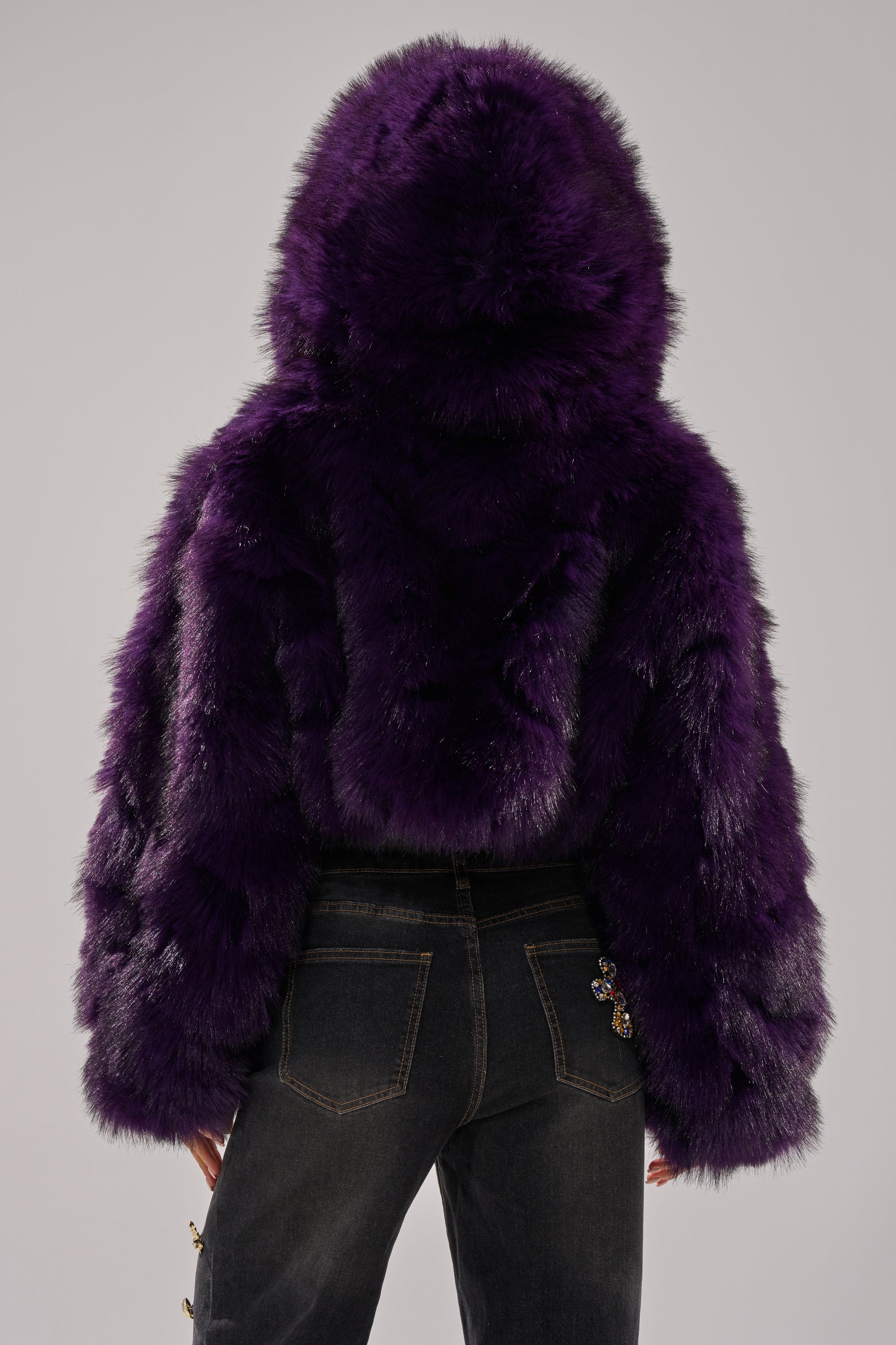 A person wearing the JUST A FLING CROPPED FAUX FUR jacket in plush deep purple and dark jeans, shown from the back against a plain light background.