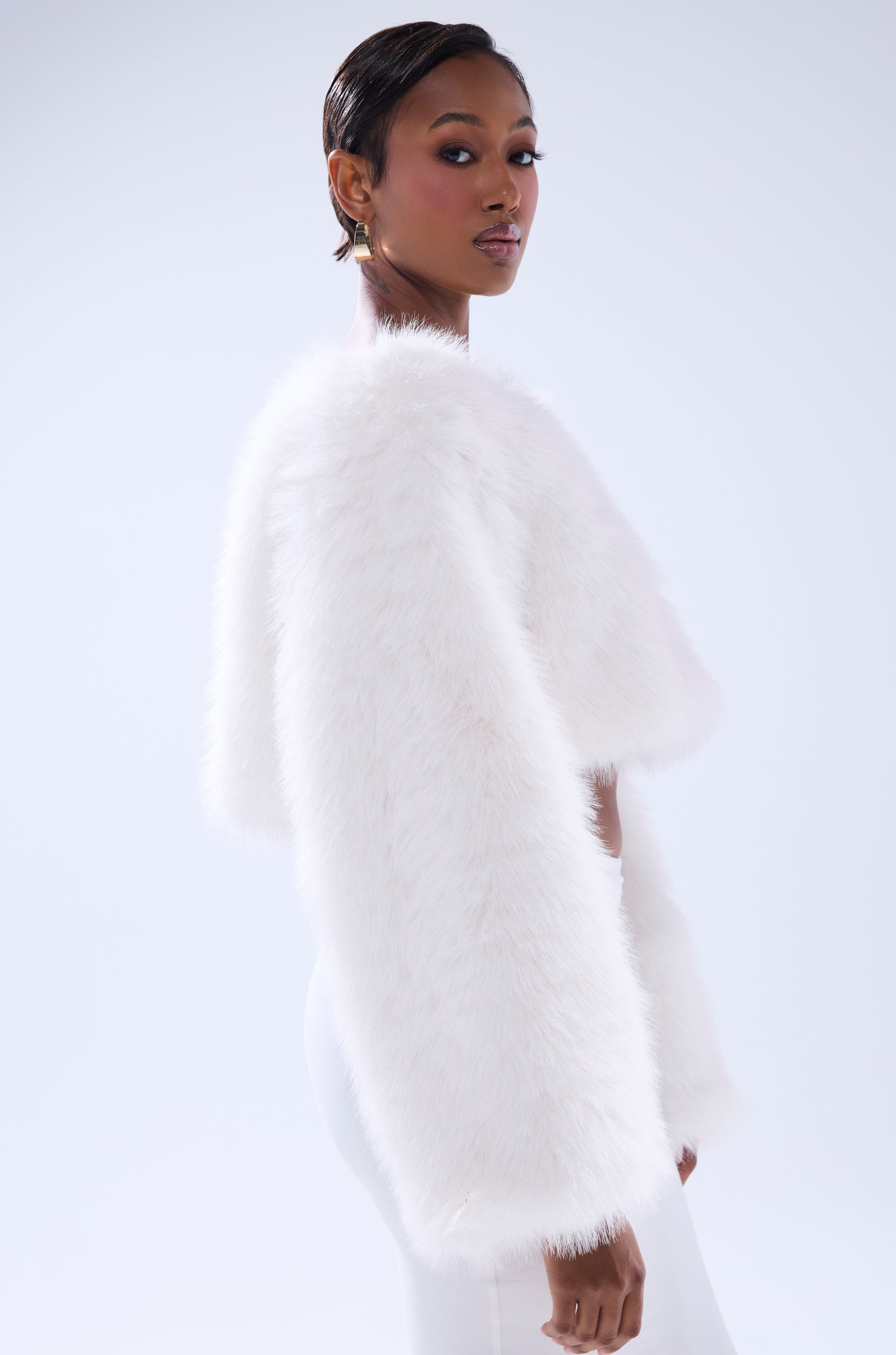 A woman with short, slicked-back hair poses confidently in the COMFY COZY CROPPED SWEATER—white, fluffy faux fur—paired with matching pants against a plain, light background.