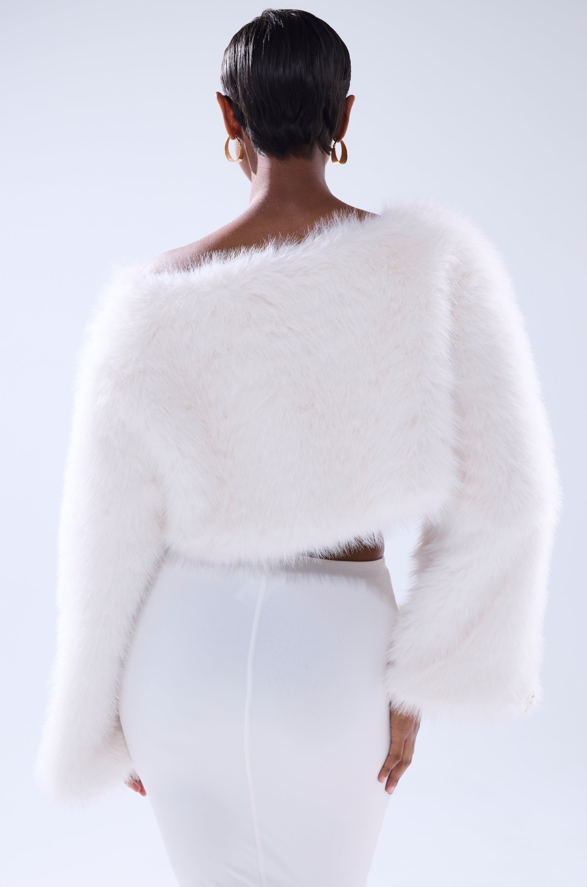 A woman with short hair, seen from behind, wears gold hoop earrings and the COMFY COZY CROPPED SWEATER against a plain light background.