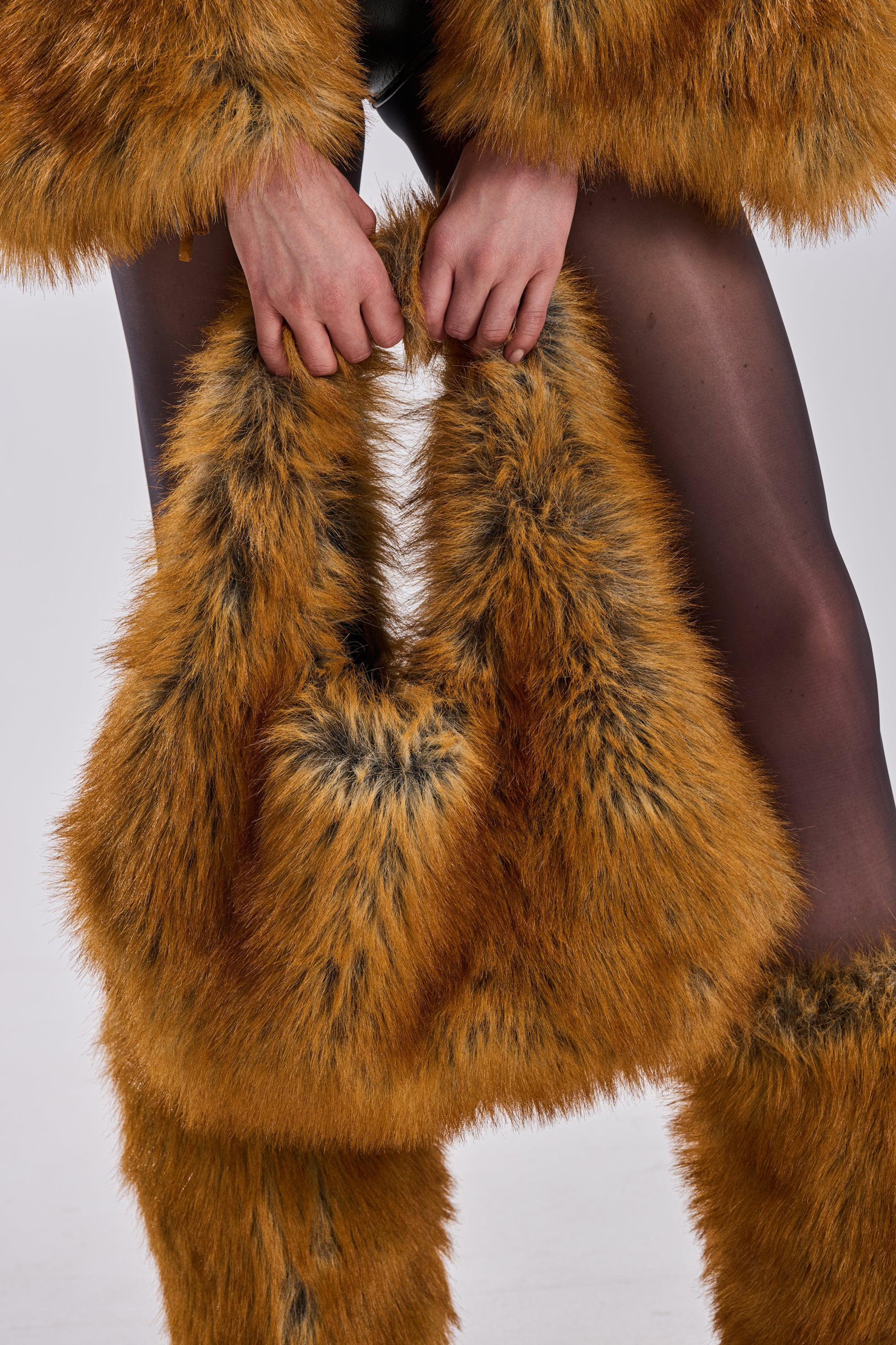 A person with only their hands and legs visible wears black sheer tights, orange and black-tipped faux fur clothing, and holds the REALLY LIKE THAT FAUX FUR MINI TOTE against a plain background.
