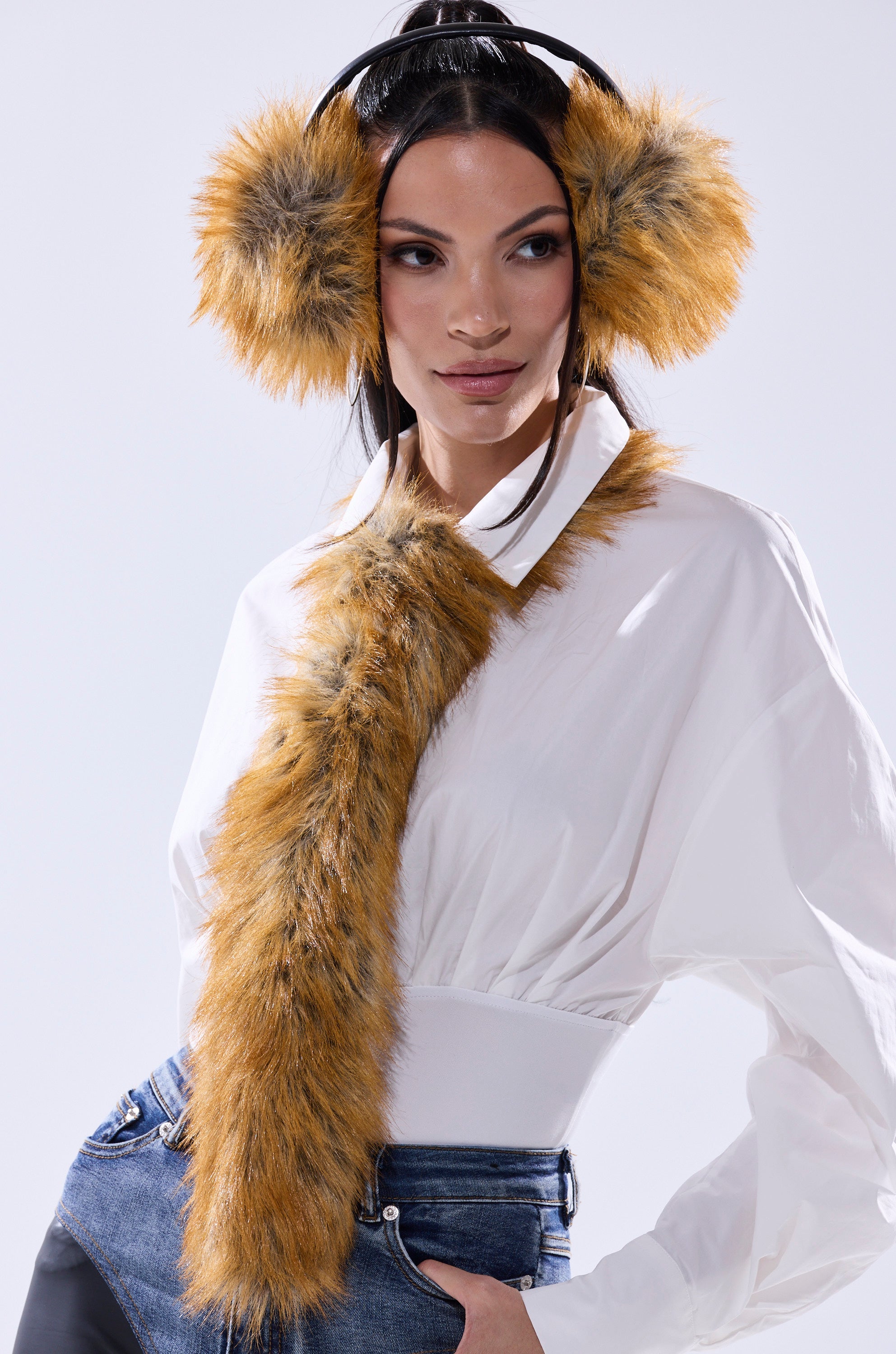A woman wears the REALLY LIKE THAT FAUX FUR TIE and fluffy orange-brown AKIRA Label earmuffs over a white blouse and blue jeans, standing against a light background. 4