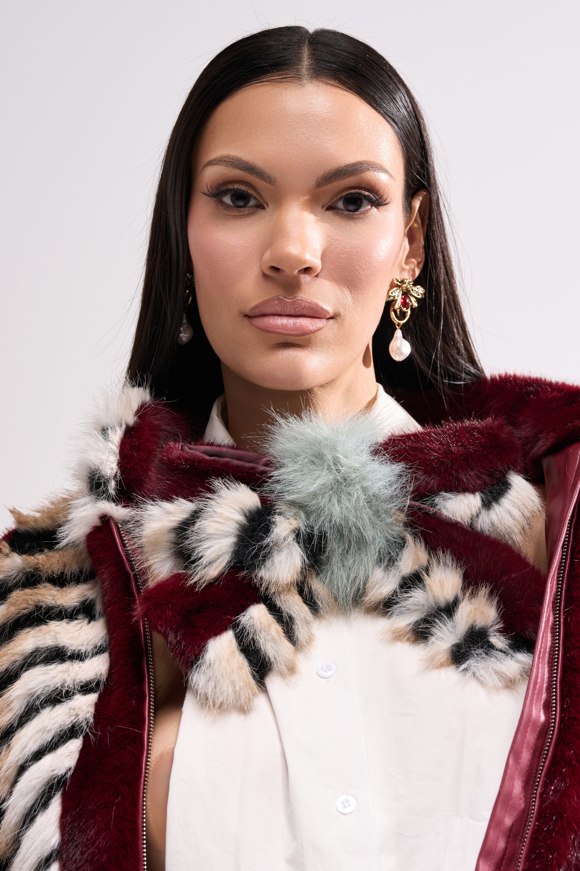 A woman with long dark hair, styled with the HAVE IT ALL FAUX FUR HAIR CLIP, wears statement earrings, a white shirt, and a patterned fur scarf, gazing confidently at the camera against a light background.