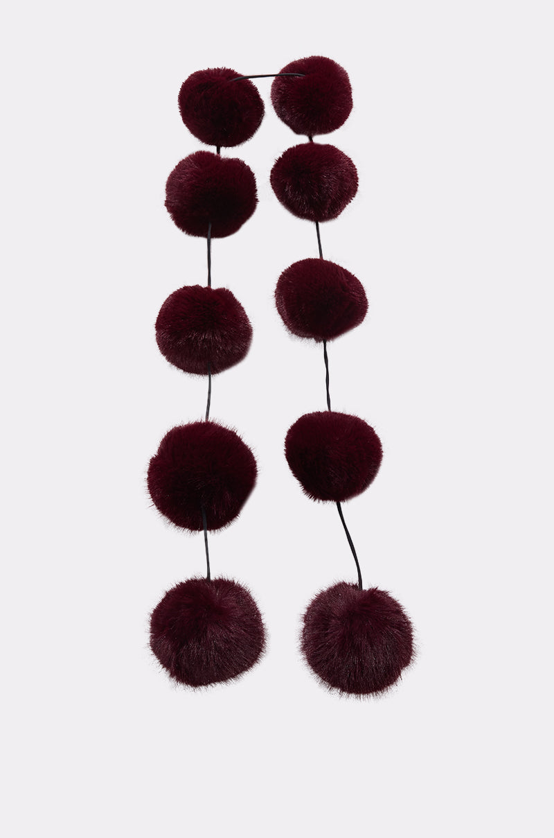 The FEELIN BALLSY FAUX FUR SCARF features large, dark burgundy faux fur pom-poms in a single line, channeling a cozy, oversized scarf style, displayed against a plain white background. 4