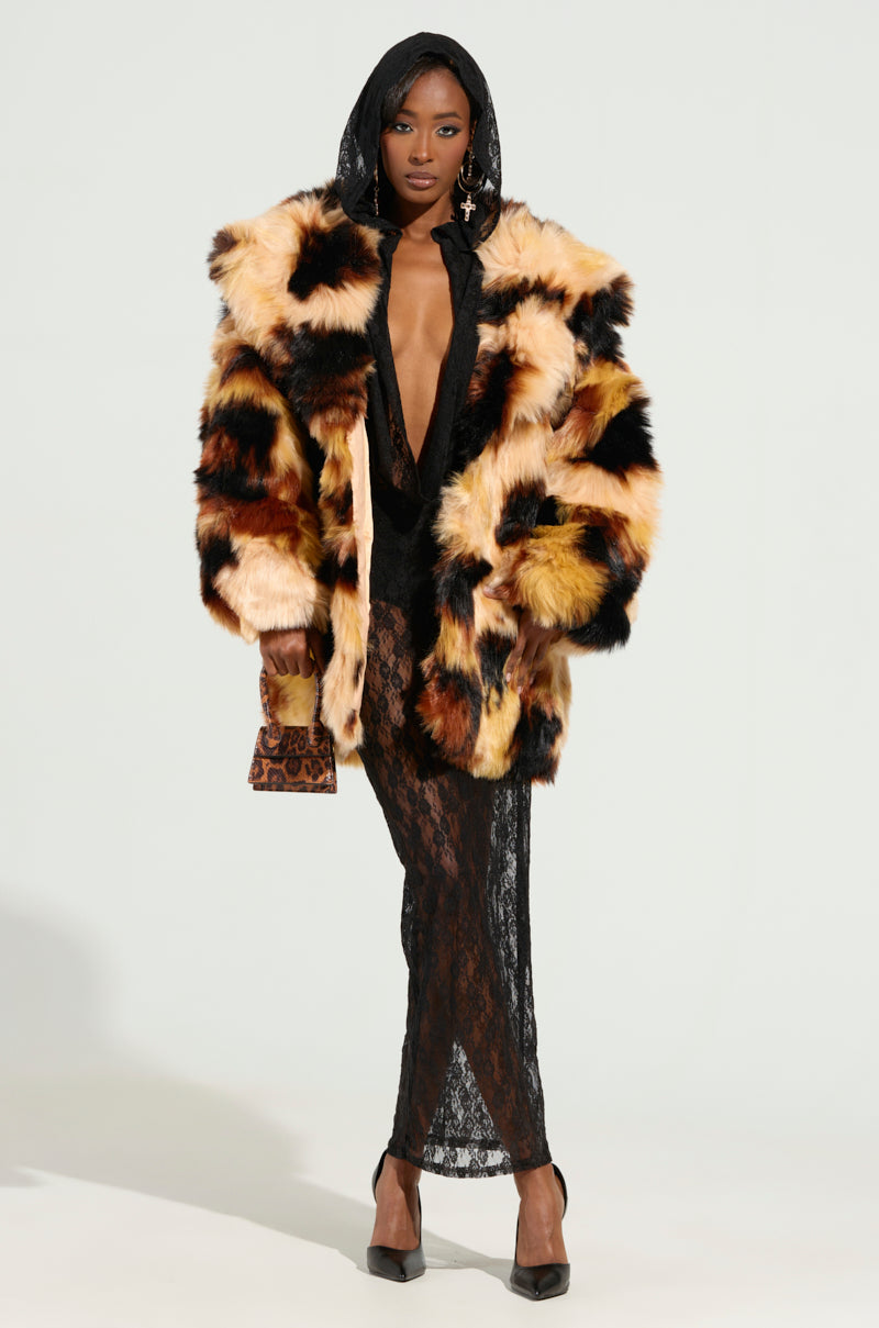 A person wearing the ARI OVERSIZED FUR COAT over a black lace dress poses with a small animal print purse. They have long earrings and are standing against a light-colored background, exuding elegance with every detail, including the purse's satin-lined interior.