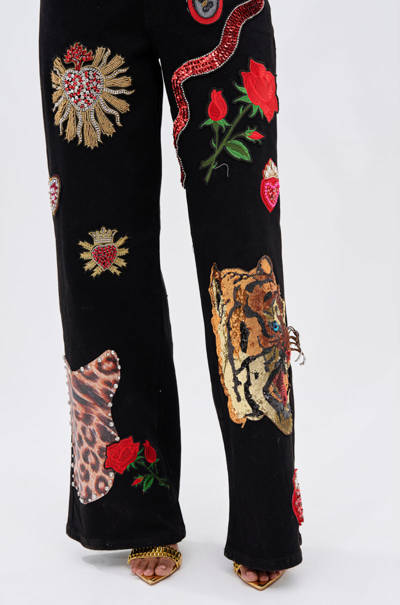 Wearing the FIERCE DENIM PANT with embroidered lion head, roses, leopard print, red snake, and jeweled heart patches makes a bold statement of rebellious glam—perfectly styled with open-toe heels.