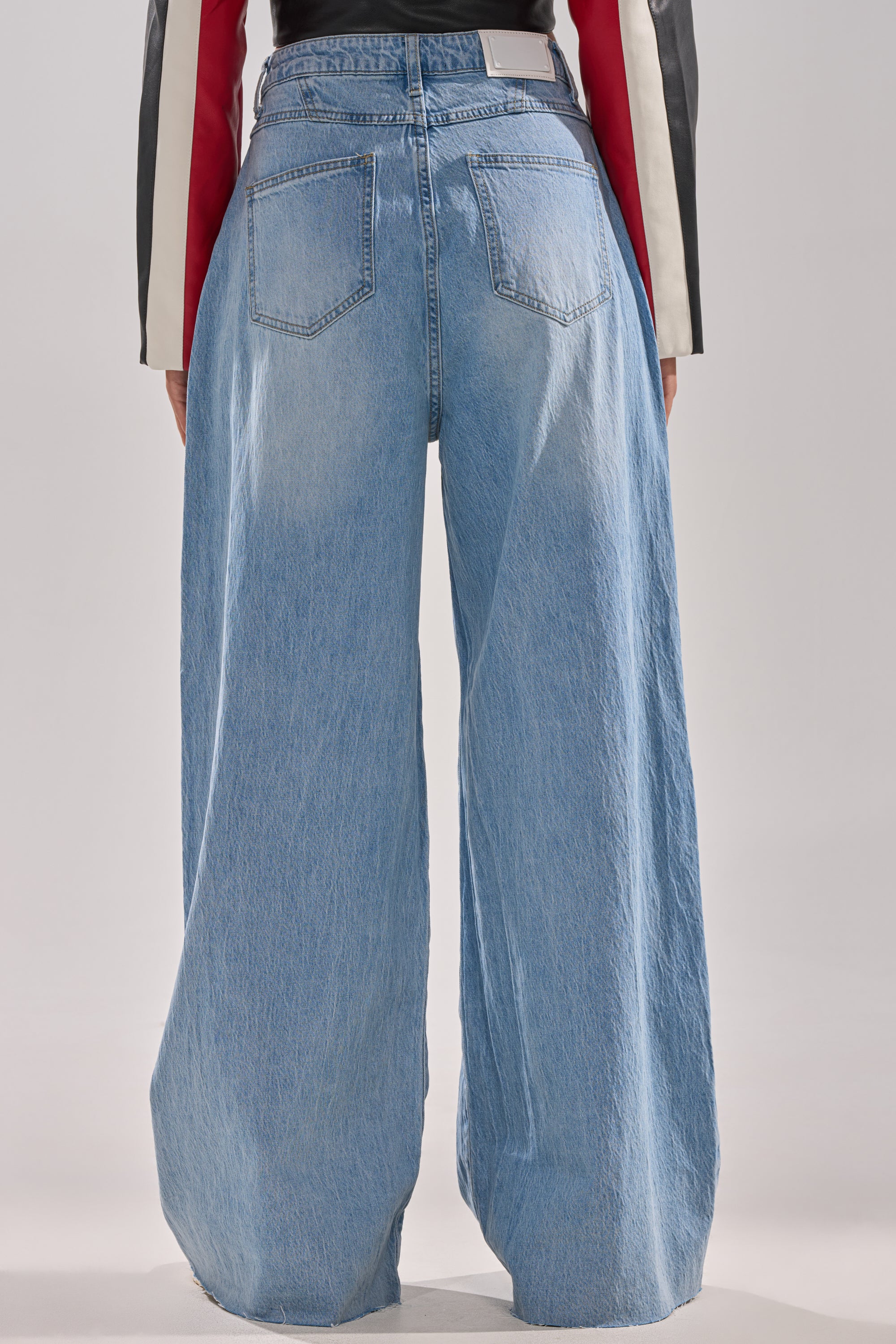 Back view of a person wearing the YOU BET DRAWSTRING WIDE LEG JEANS in light blue vintage wash with two back pockets, floor-length fit, styled with a black, red, and white long-sleeve top.