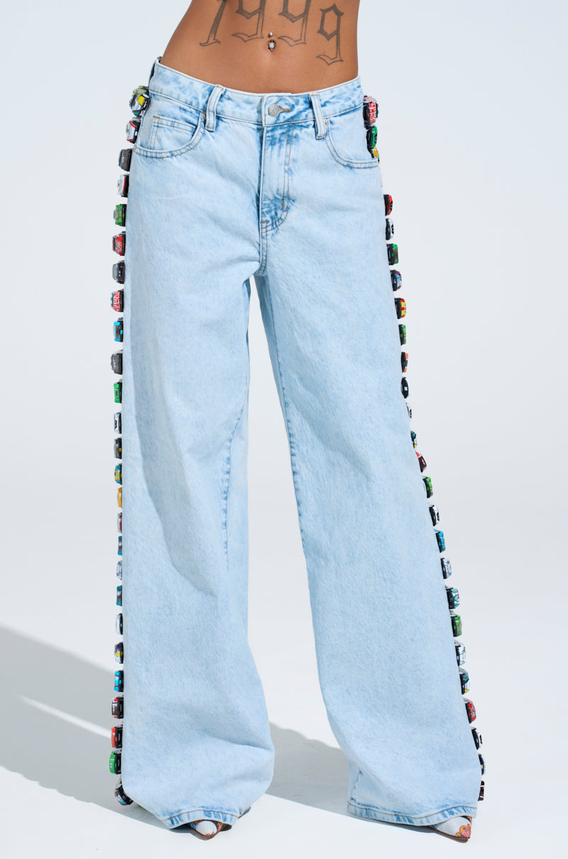 In light wash RACE CAR JEANS with colorful race cars lining the seams, a person stands out against a plain background, showcasing a "1999" tattoo across their stomach.