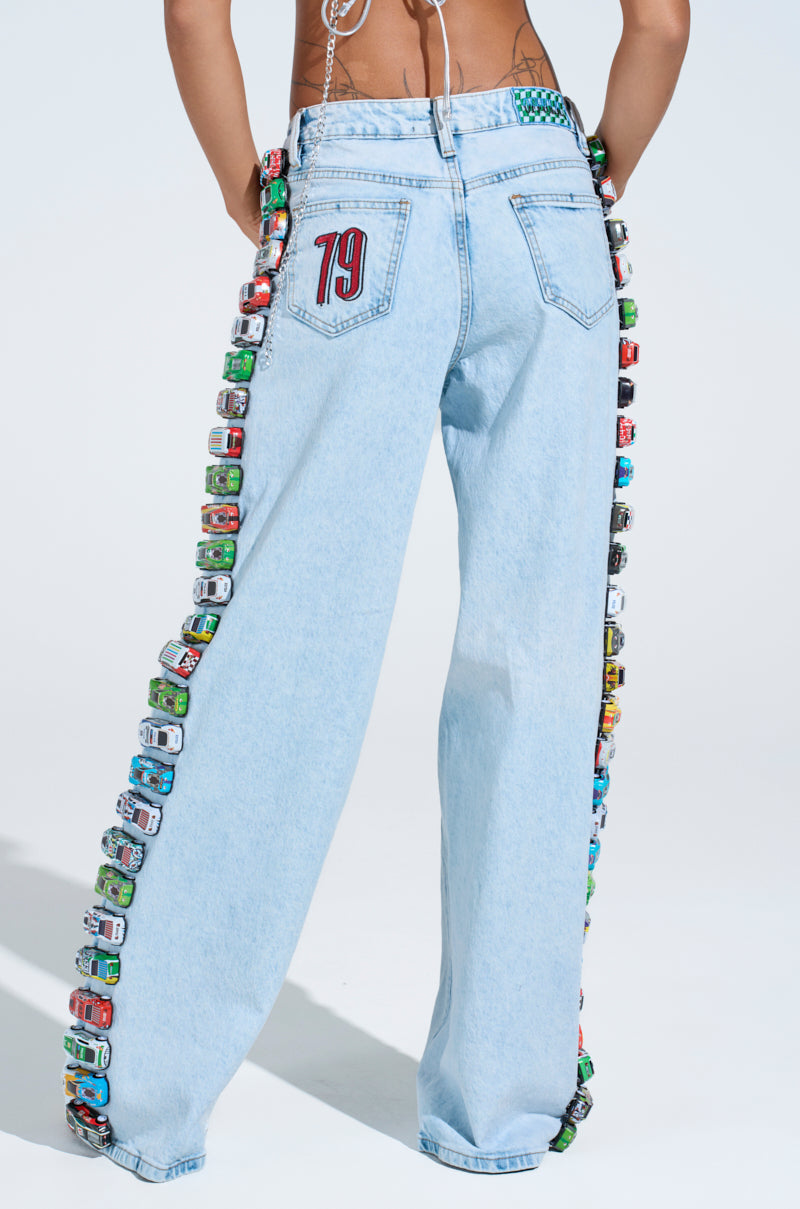 Dressed in relaxed light wash wide-leg RACE CAR JEANS, featuring miniature toy cars down the seams and a bold red "19" on a plain white back pocket.