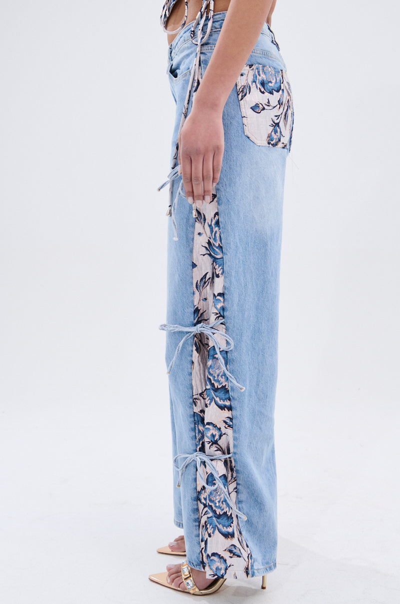 A person wears SEASONAL AWAKENING BROCADE PATCH DENIM JEANS—high-rise wide-leg denim with floral brocade panels and tie details—paired with beige heeled sandals. Side shot captures waist to feet. 4