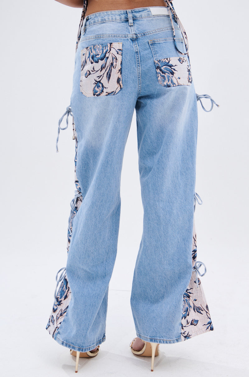 A person wears SEASONAL AWAKENING BROCADE PATCH DENIM JEANS—light blue, high-rise wide-leg jeans with floral brocade patches on the back pockets and sides—styled with nude heels for a chic, relaxed look. 6